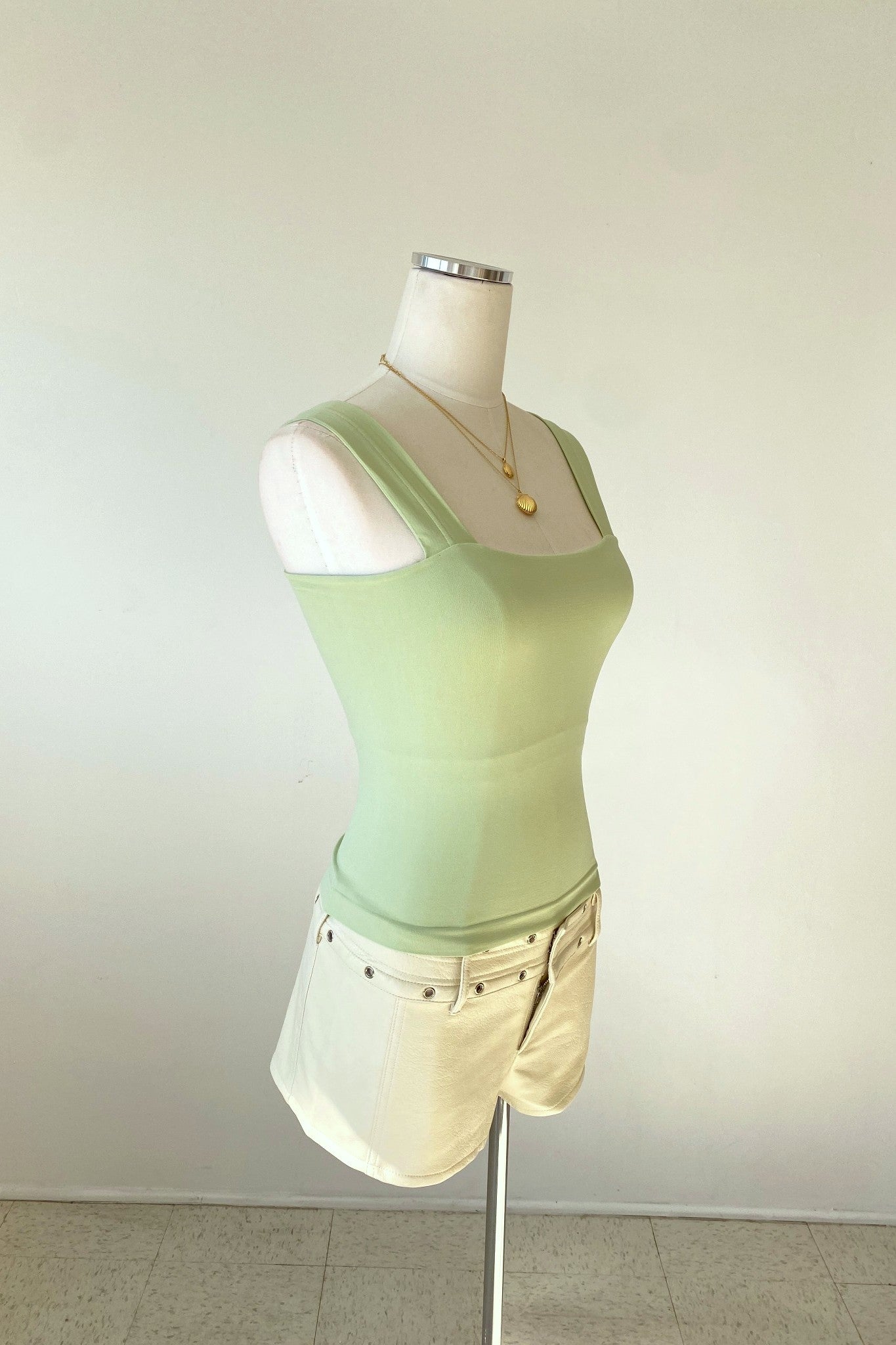 Mannequin wearing a light green tank top and white shorts on a plain background