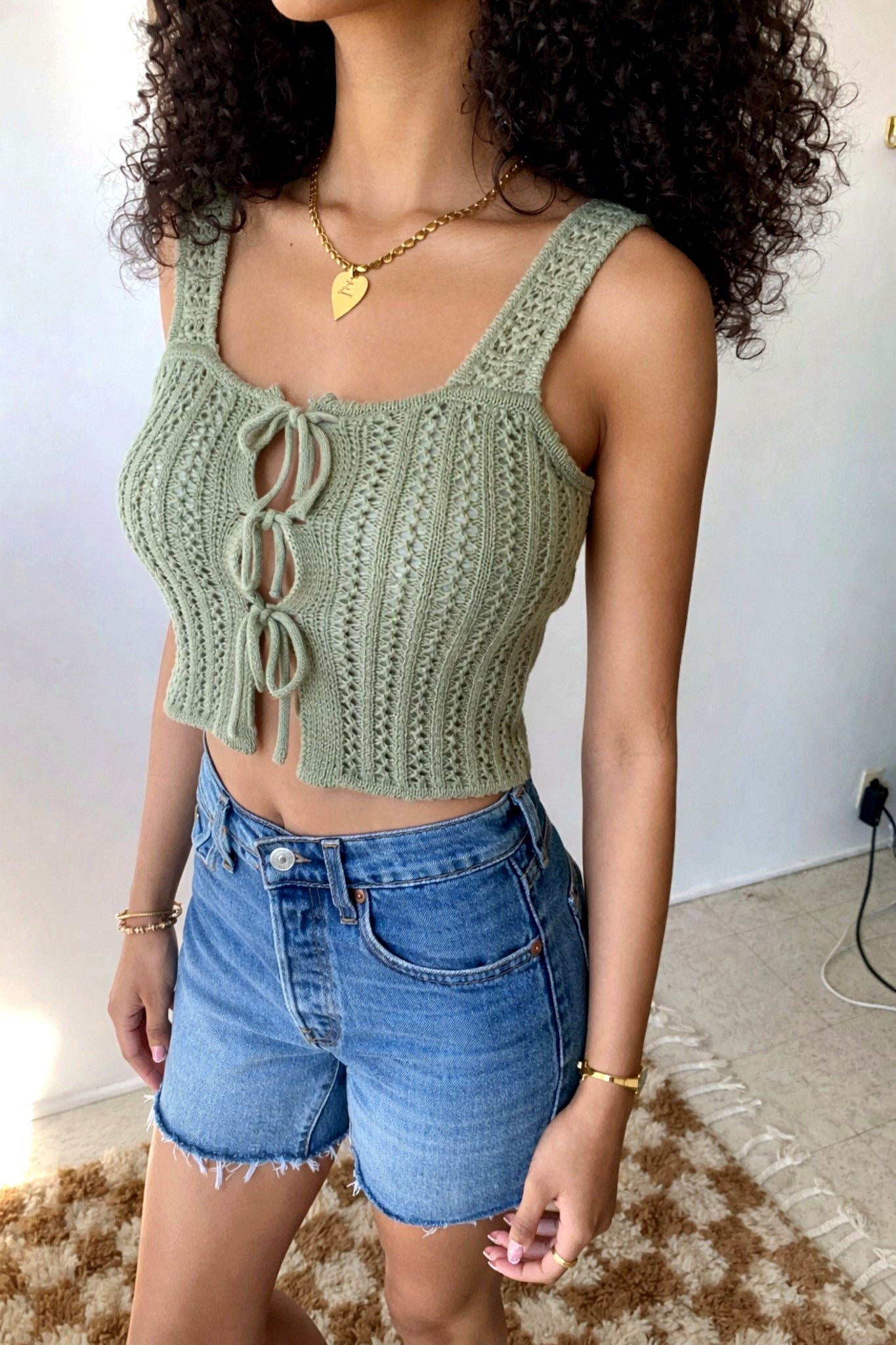 Woman wearing a green knitted crop top and blue shorts indoors.
