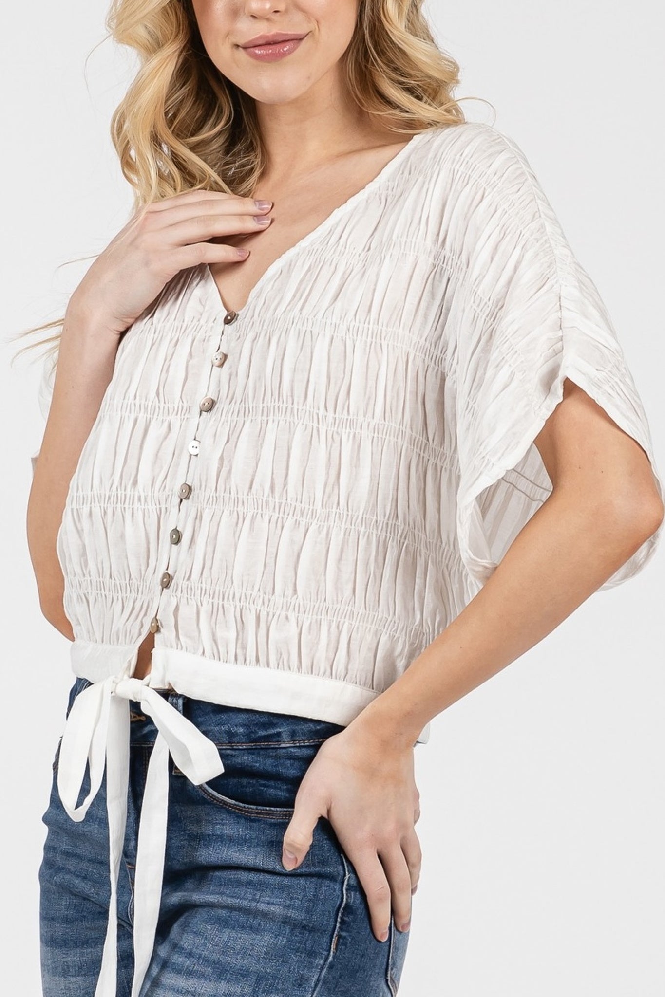Woman wearing a white textured top and blue jeans on a white background