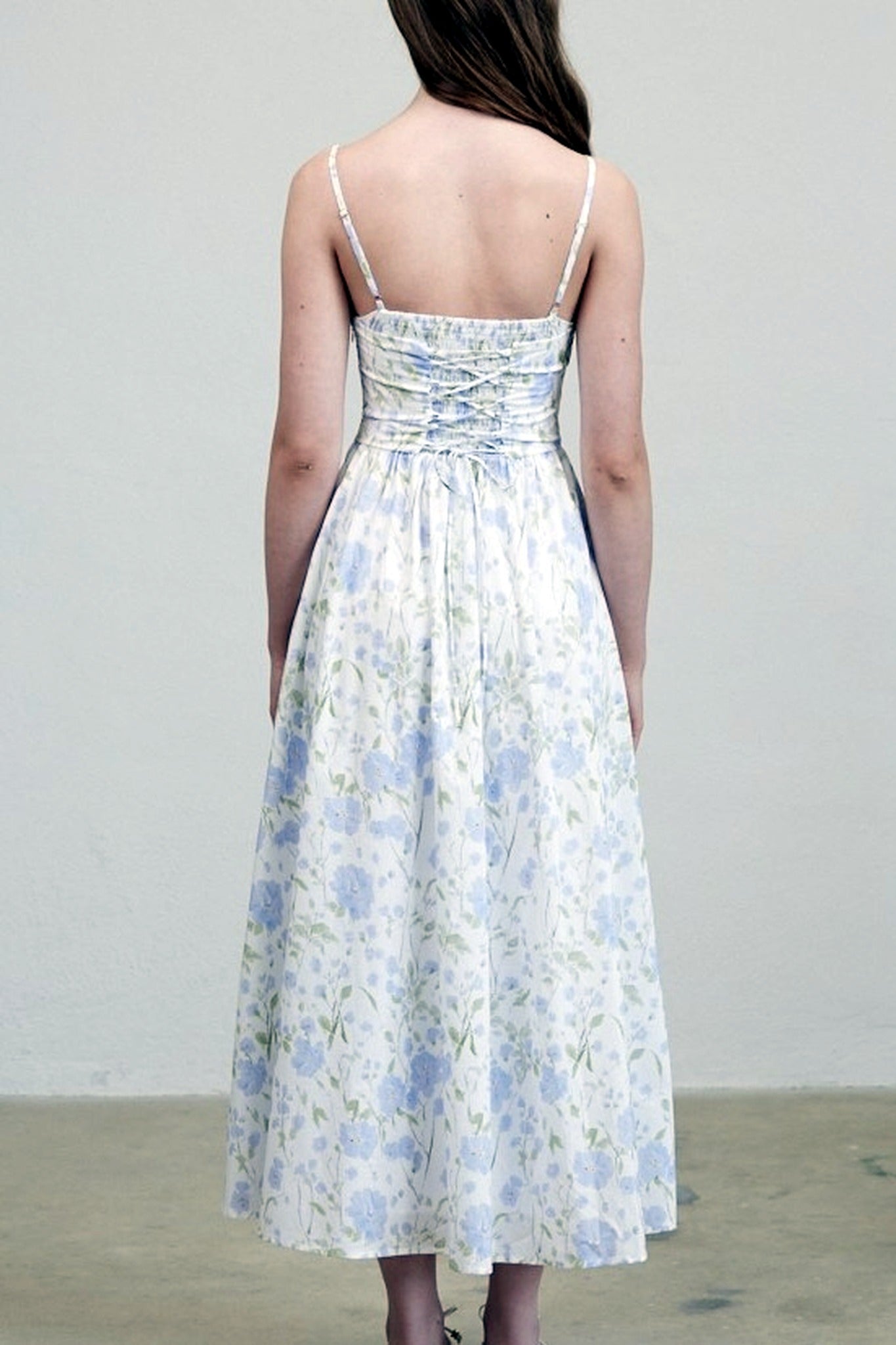 Woman wearing a floral dress with thin straps against a plain background