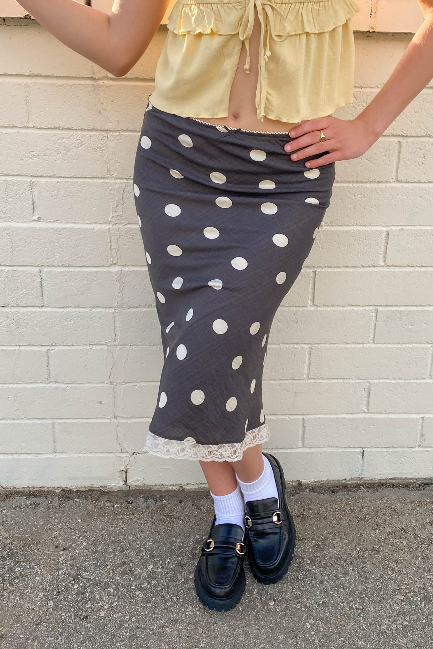 Person wearing a polka dot skirt and yellow top against a brick wall.