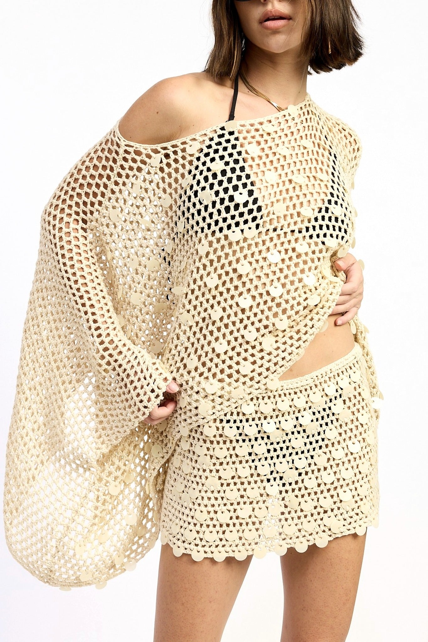 Woman wearing a beige crochet cover-up over a black bikini on a white background