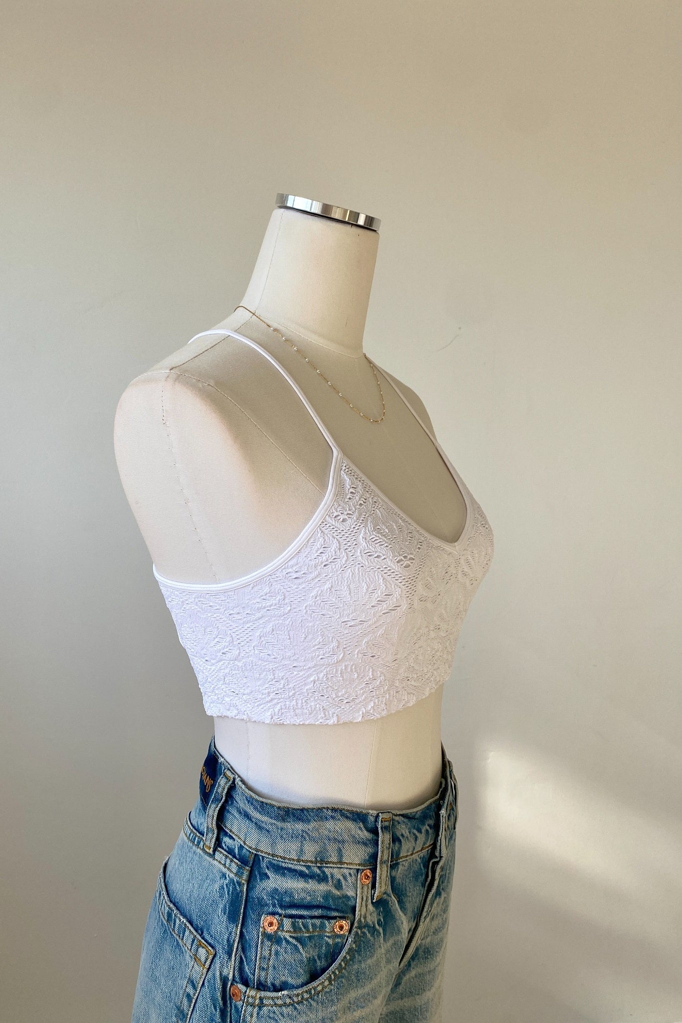 White lace crop top on a mannequin with blue jeans against a plain background