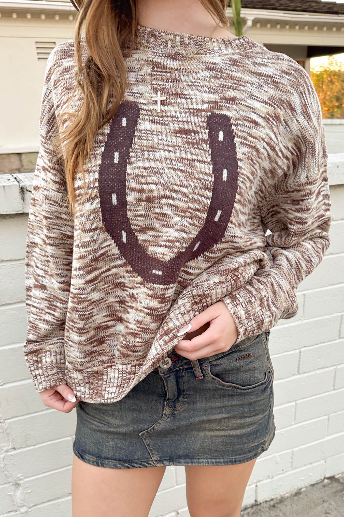Person wearing a sweater with a horseshoe design against a white brick wall.