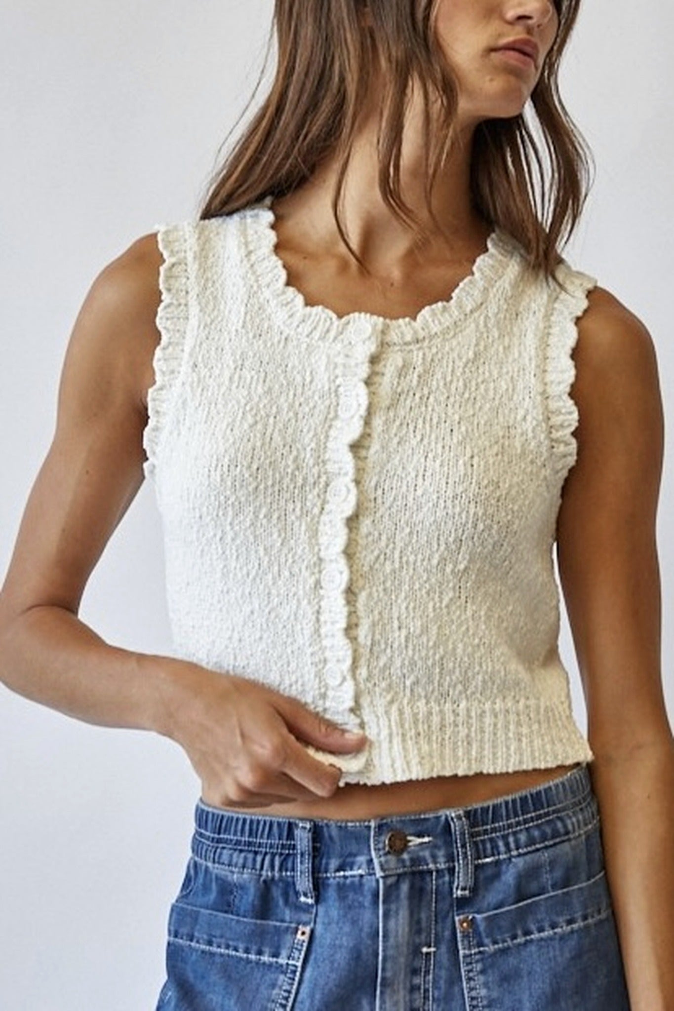 Woman wearing a textured white sleeveless top and blue jeans against a plain background