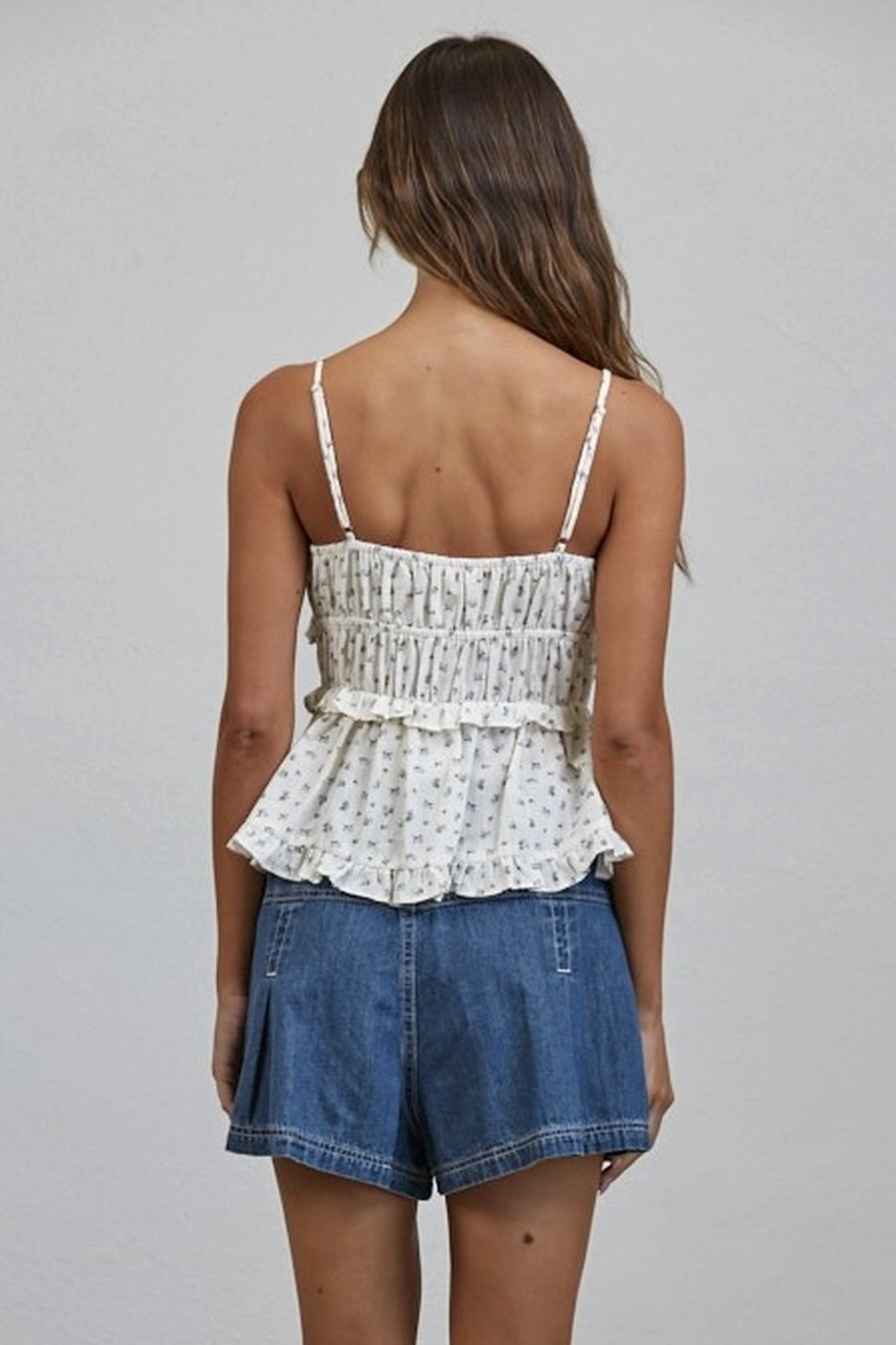 Woman wearing a floral peplum top and denim shorts on a plain background