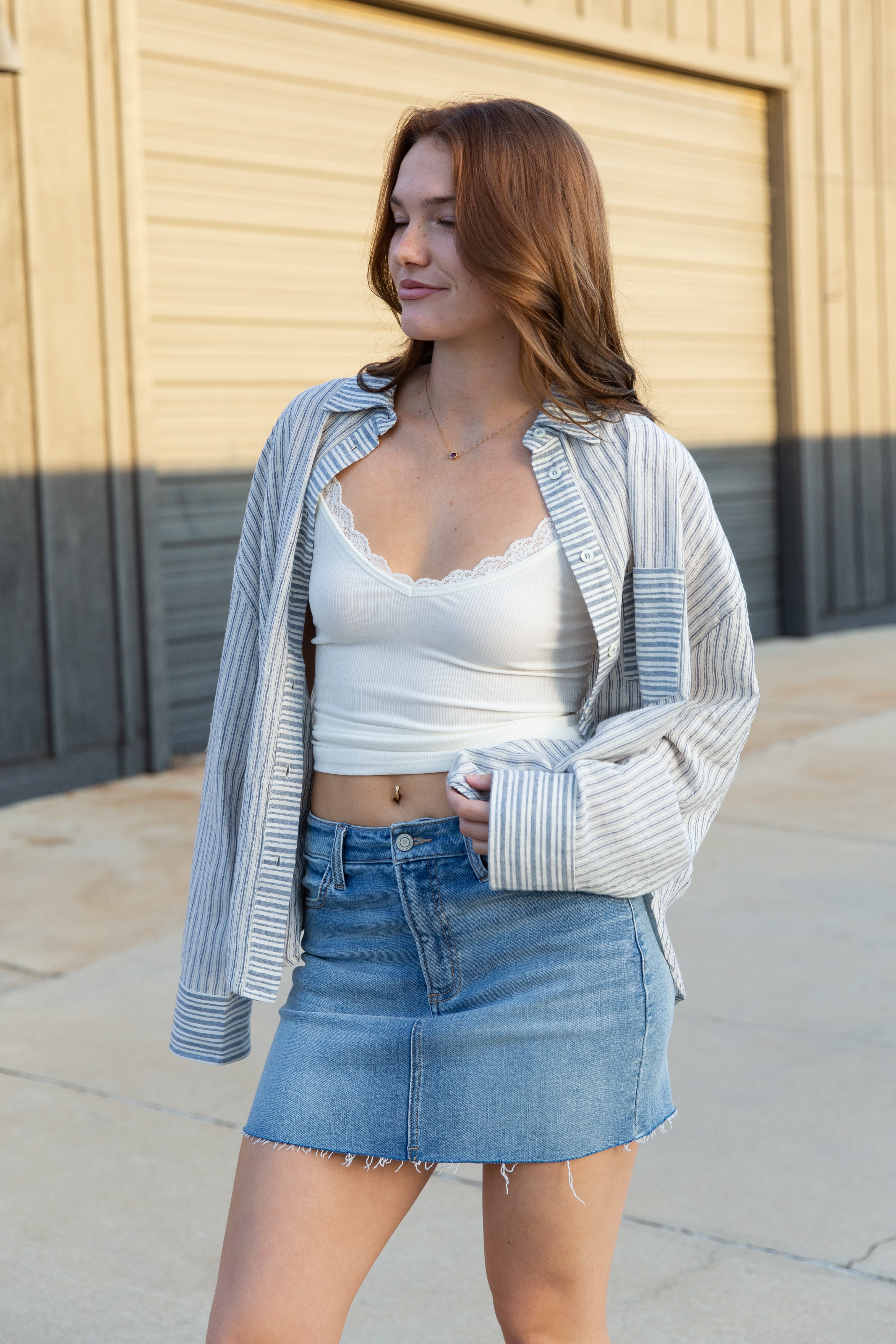 Woman wearing a white crop top, blue denim skirt, and striped cardigan in an urban setting.