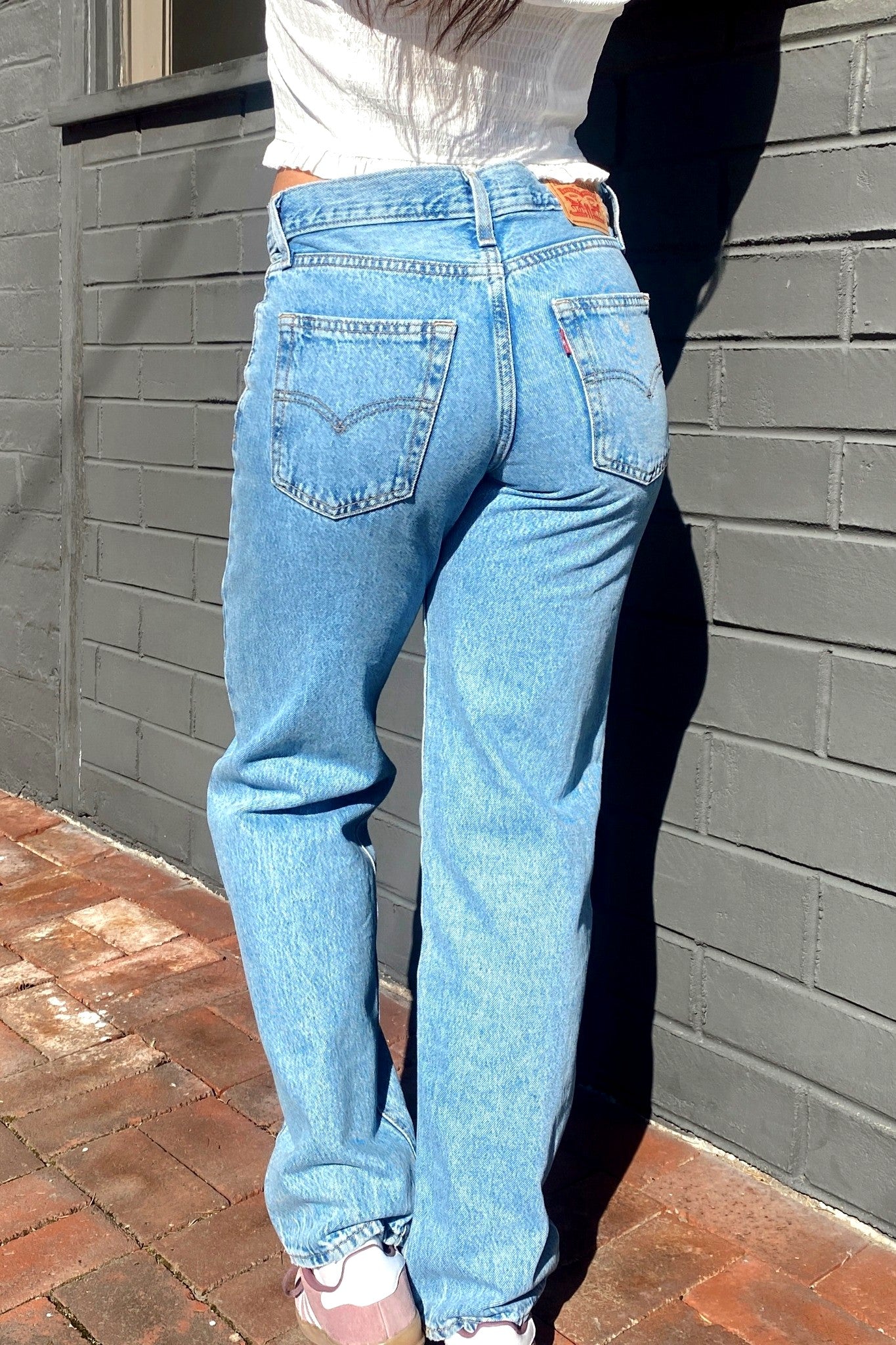 Person wearing blue jeans standing against a gray brick wall.