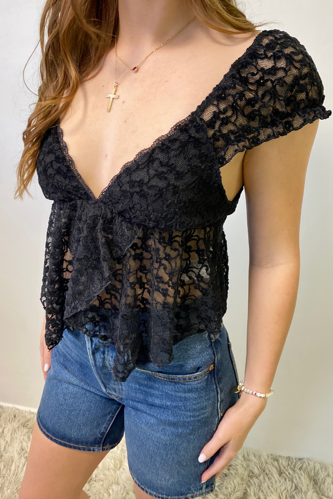 Person wearing a black lace top and denim shorts on a neutral background