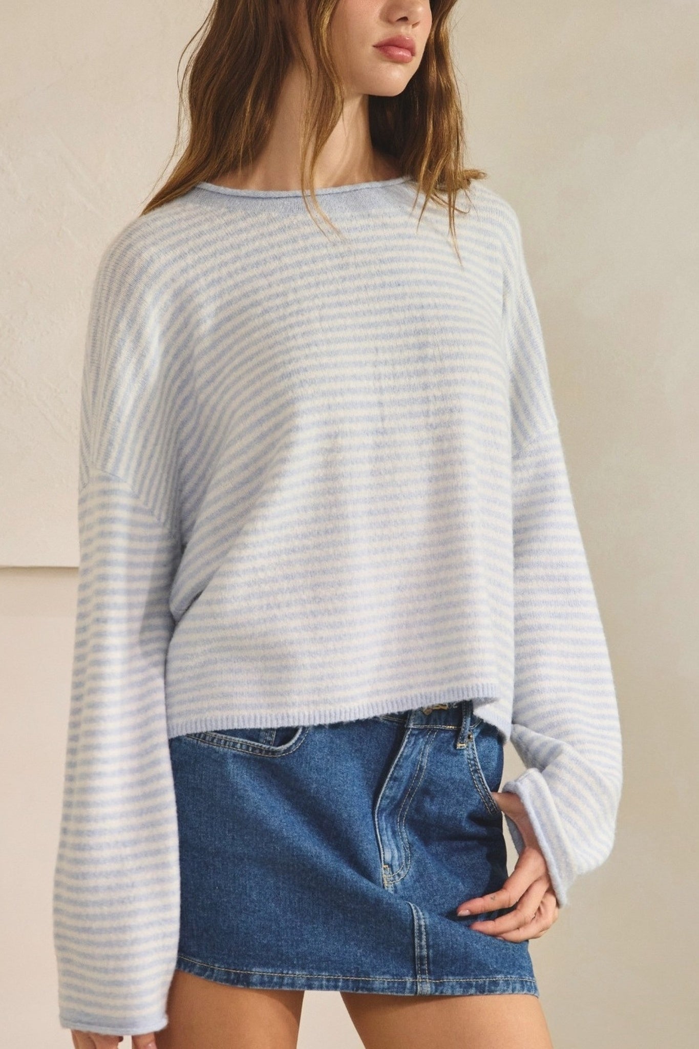 A woman wearing a light blue and white horizontally striped long-sleeve knit sweater with a wide boat neckline, paired with a blue denim mini skirt.