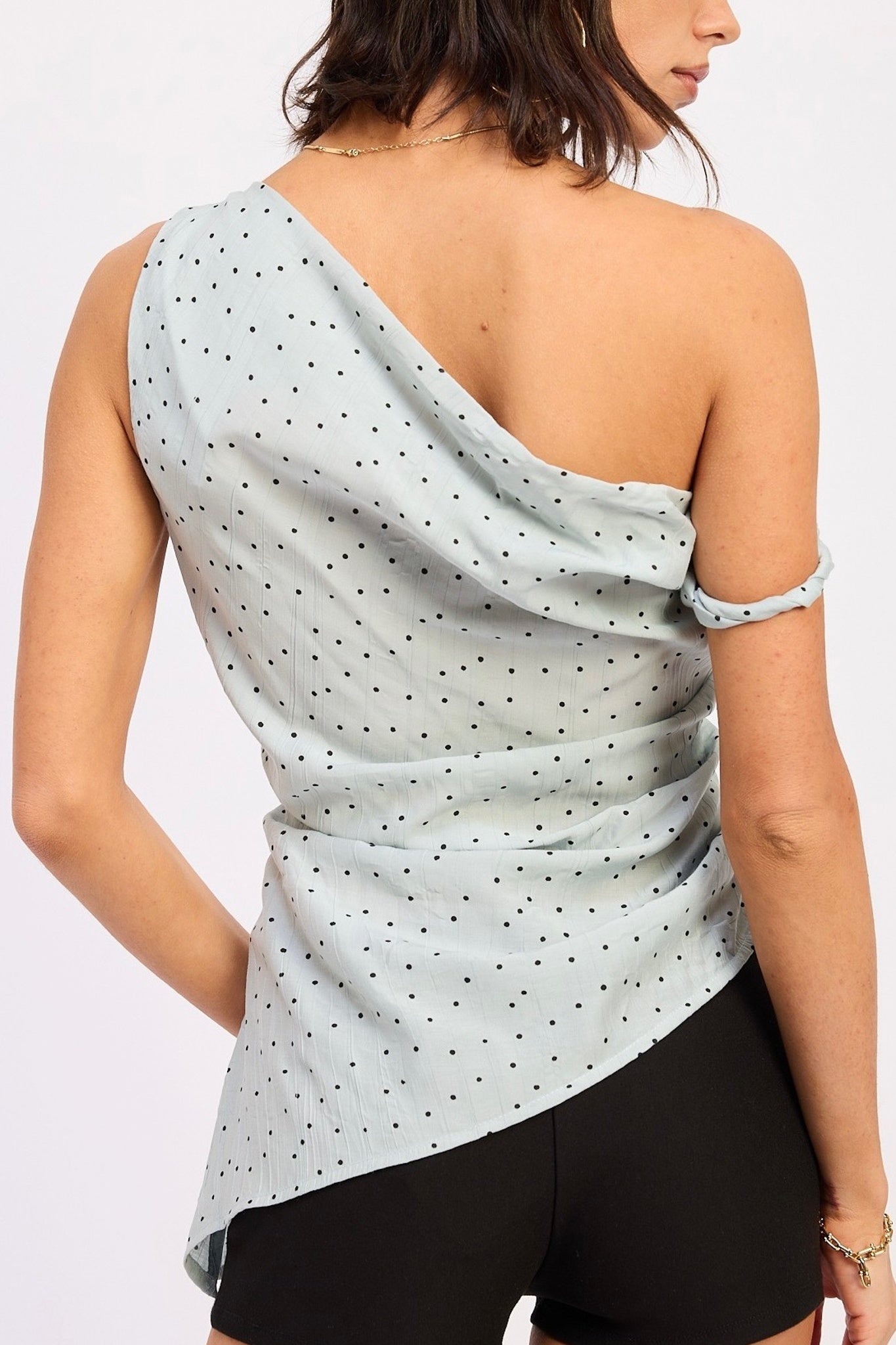Woman wearing a light blue one-shoulder top with black polka dots on a white background
