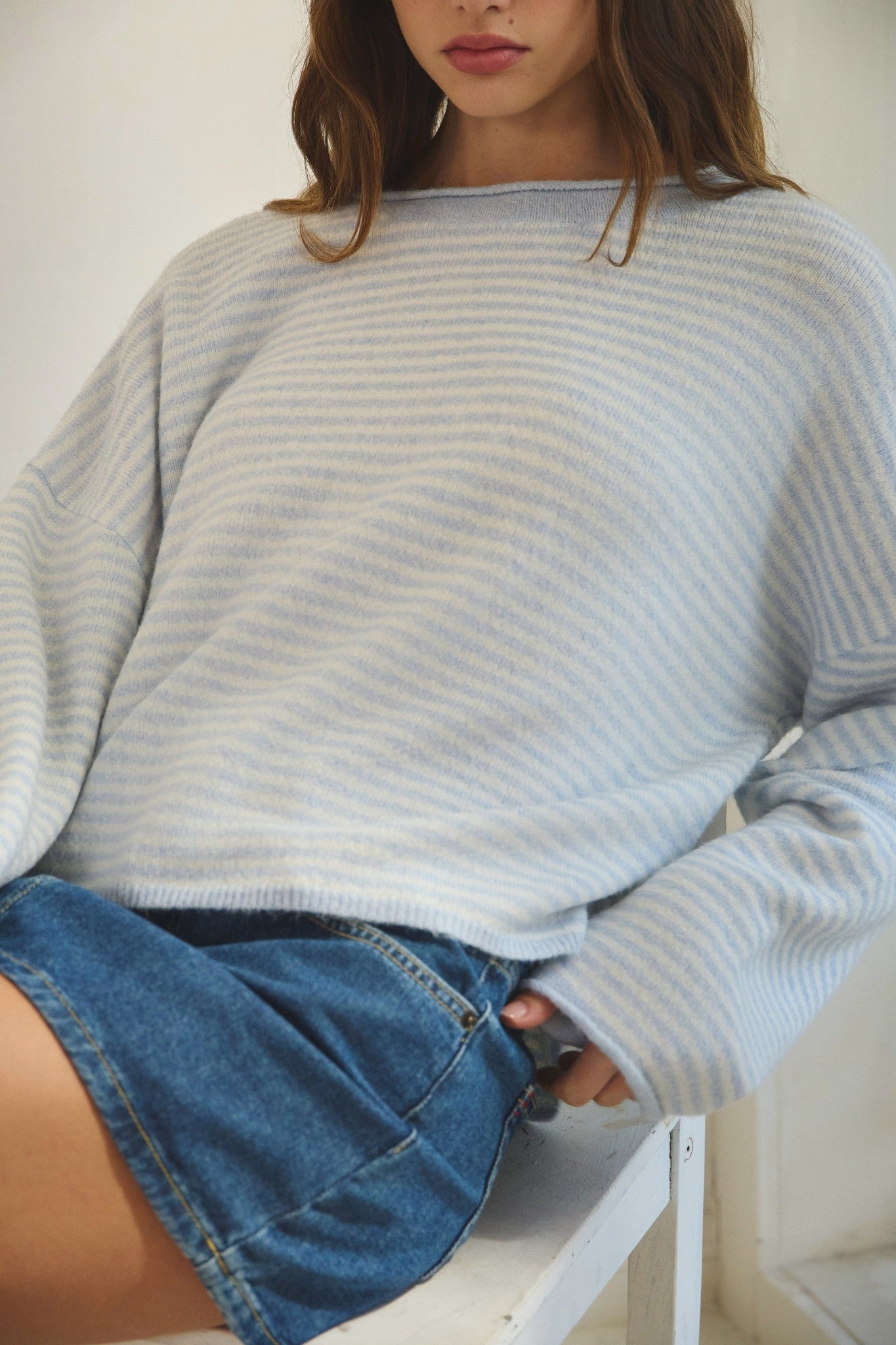 Person wearing a light blue striped sweater and denim shorts on a white background