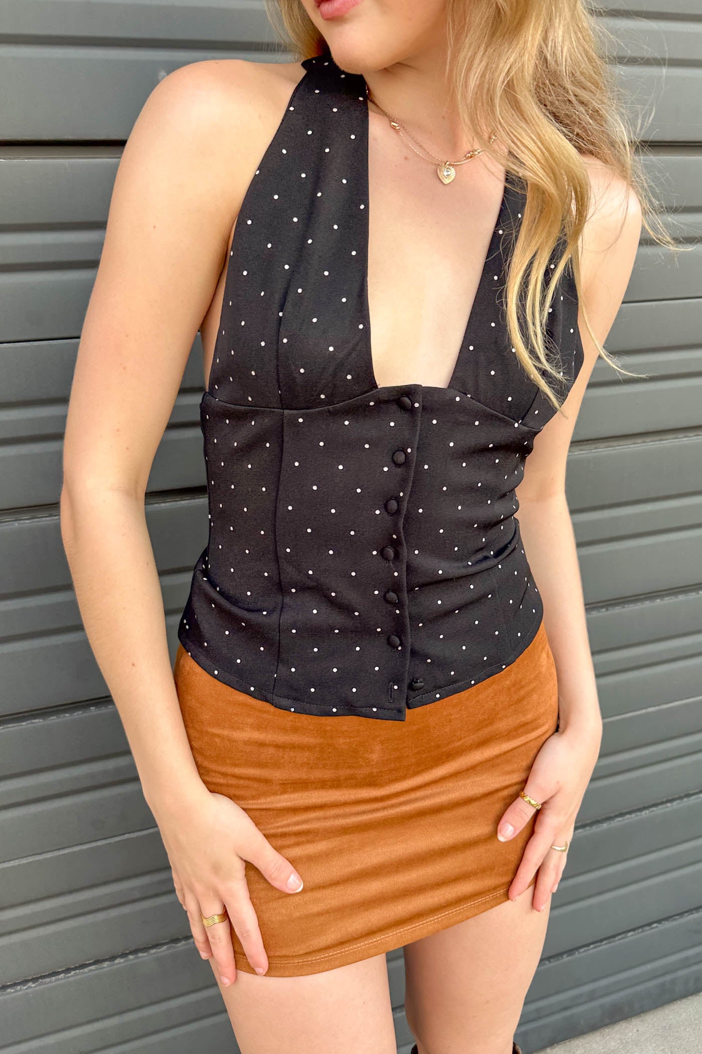Woman wearing a black polka dot top and brown skirt against a gray background