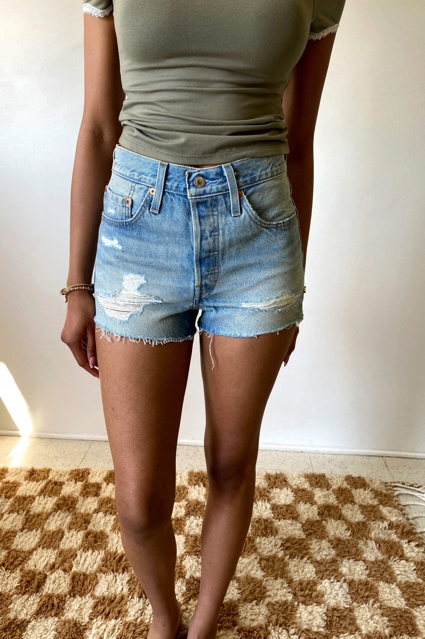 Person wearing a green top and blue denim shorts on a checkered floor.