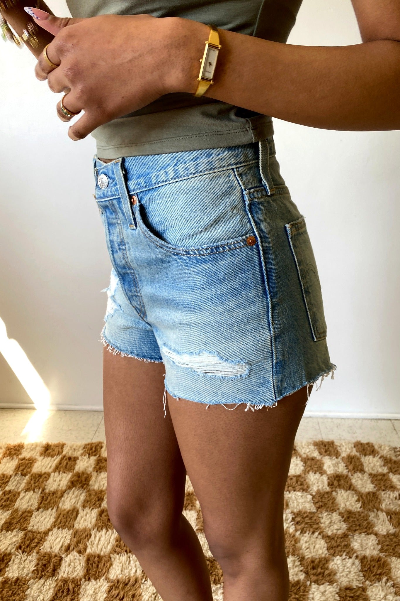 Person wearing denim shorts and a green shirt on a checkered floor.