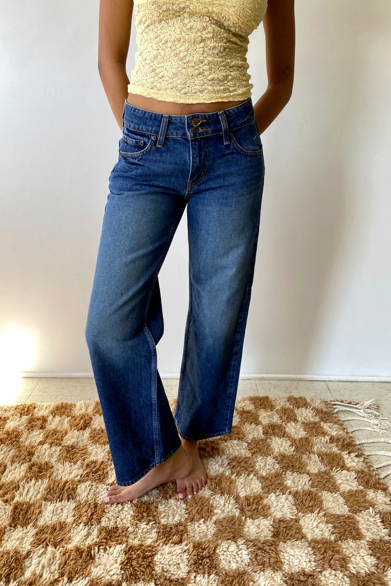 Woman wearing blue jeans standing in front of white wall.