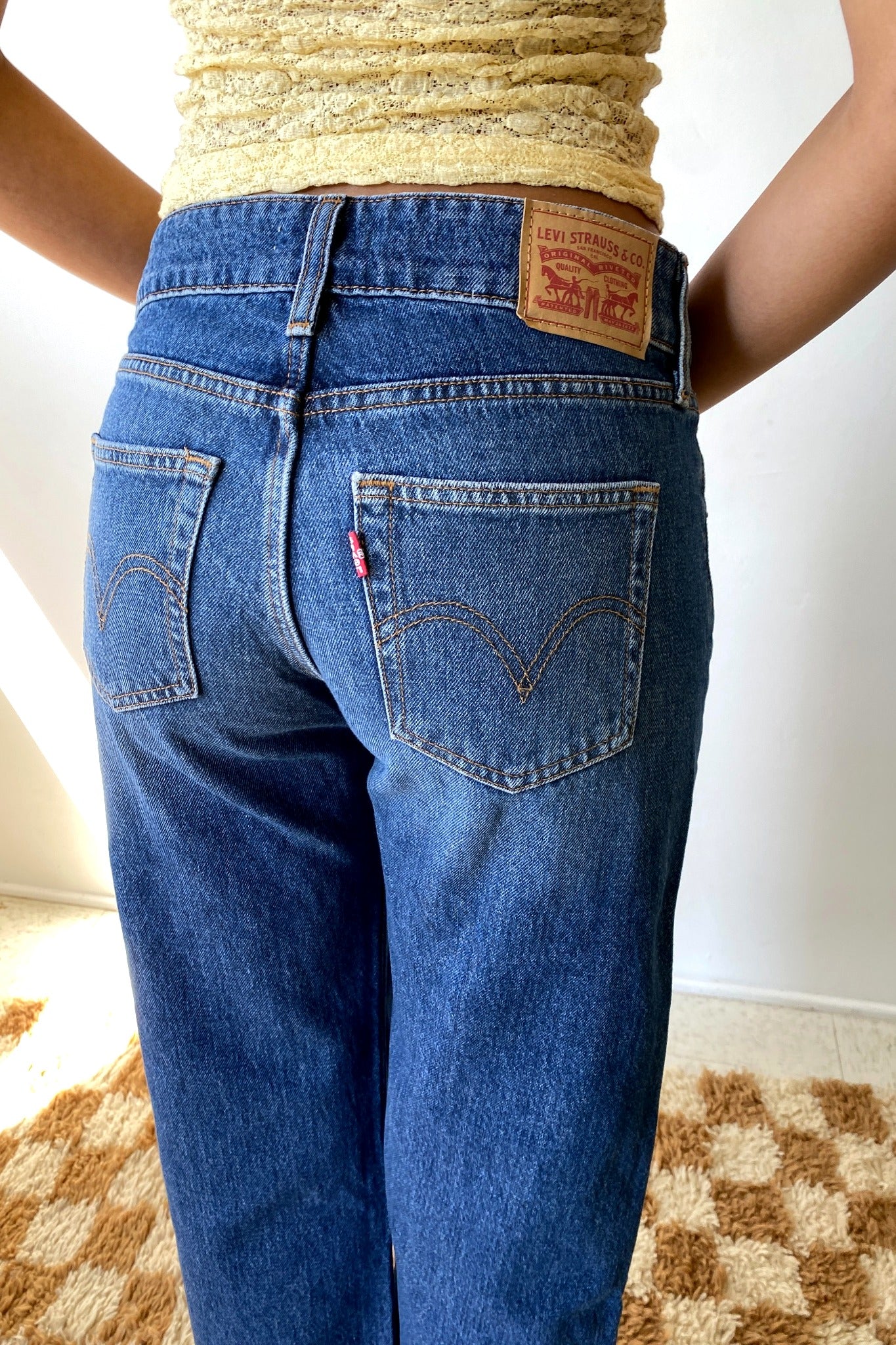 Woman wearing blue jeans standing in front of white wall.