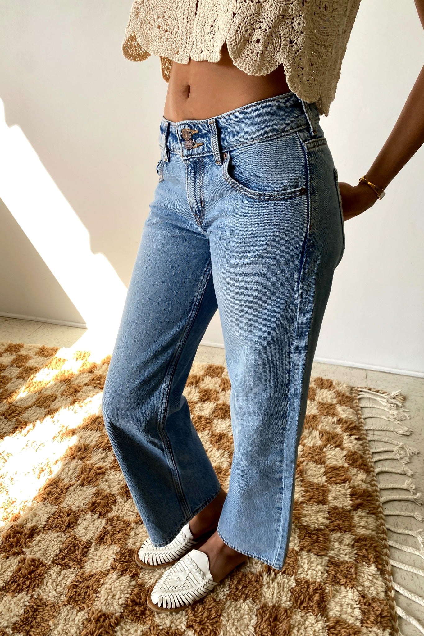 Person wearing blue jeans and a beige top on a checkered rug.
