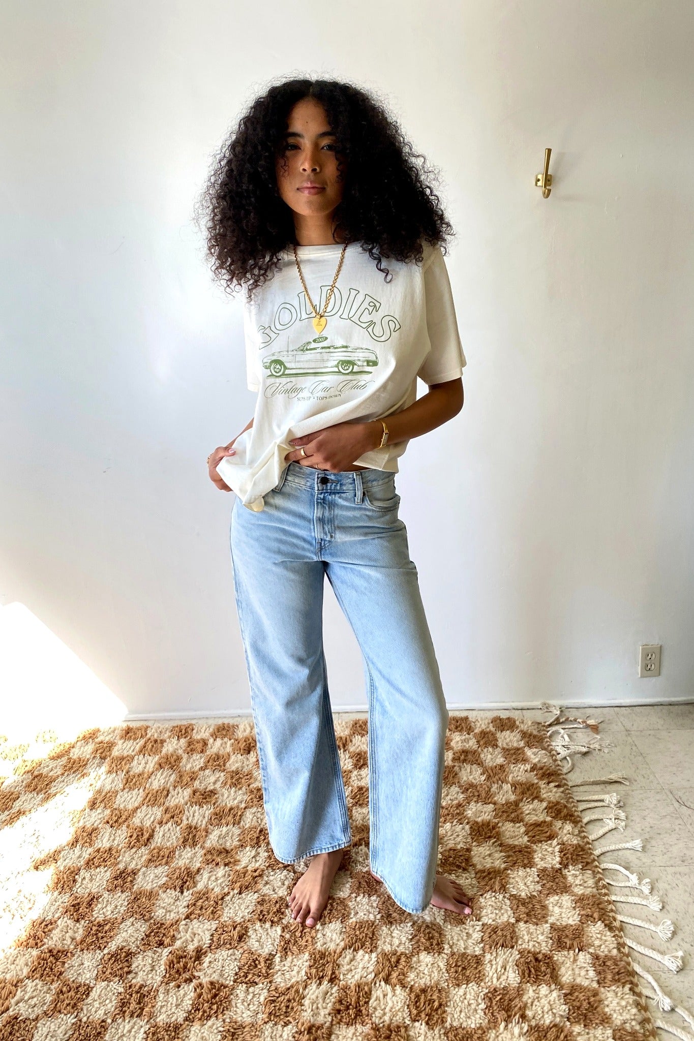 Person wearing a graphic t-shirt and light blue jeans standing on a checkered rug.