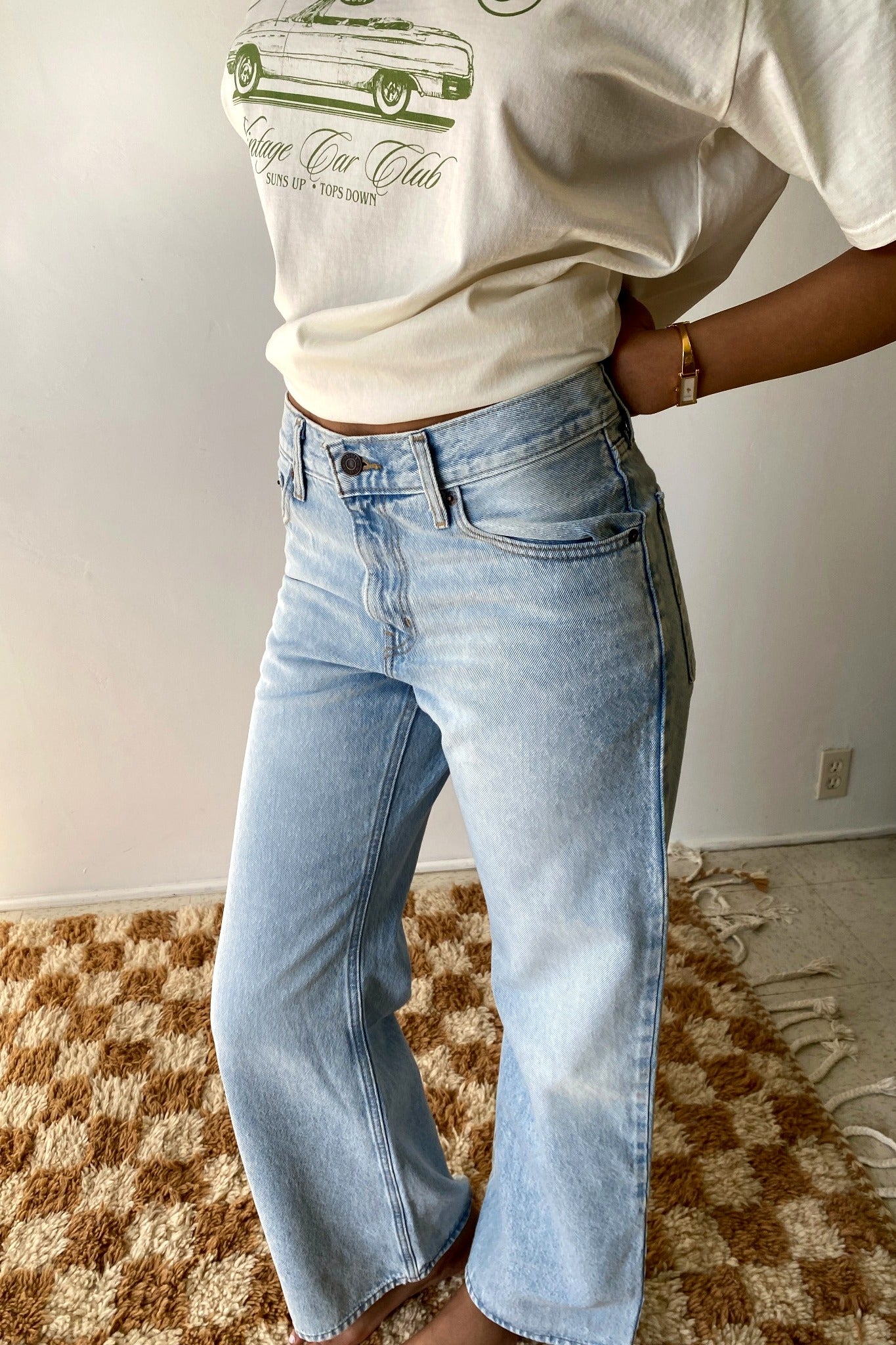 Person wearing a white t-shirt with a graphic design and light blue jeans on a checkered floor.