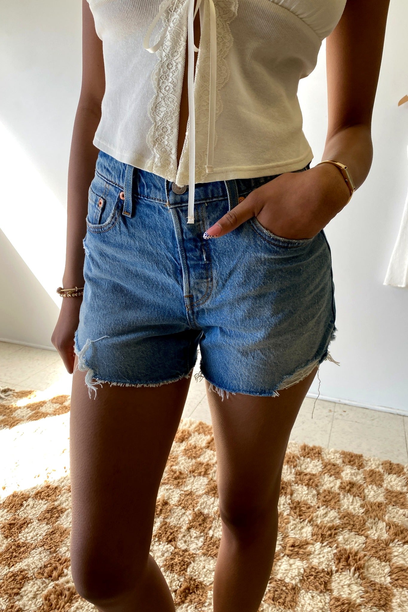 Person wearing denim shorts standing on a checkered rug indoors.
