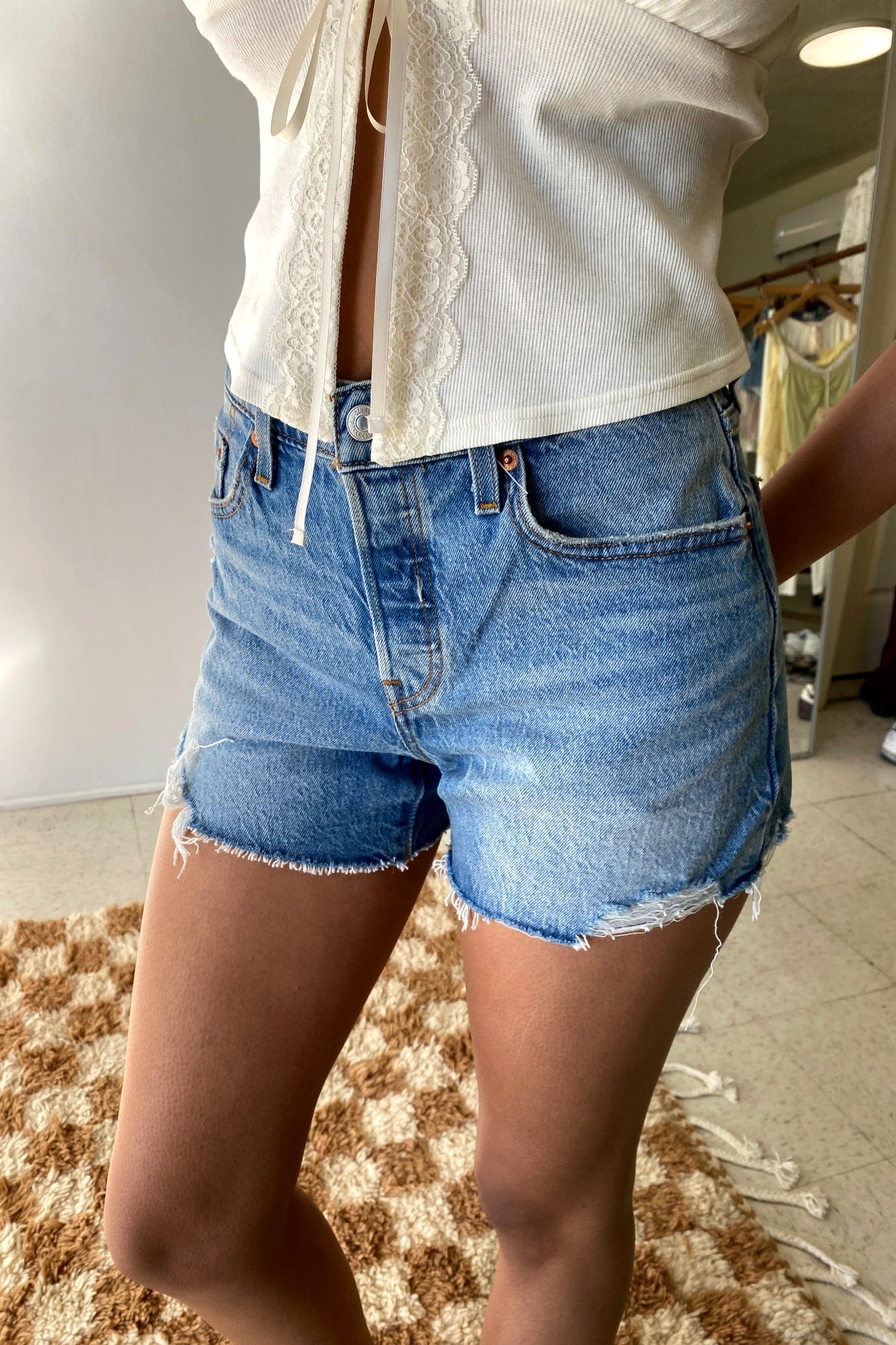 Person wearing denim shorts and a white top in a room with a checkered rug.