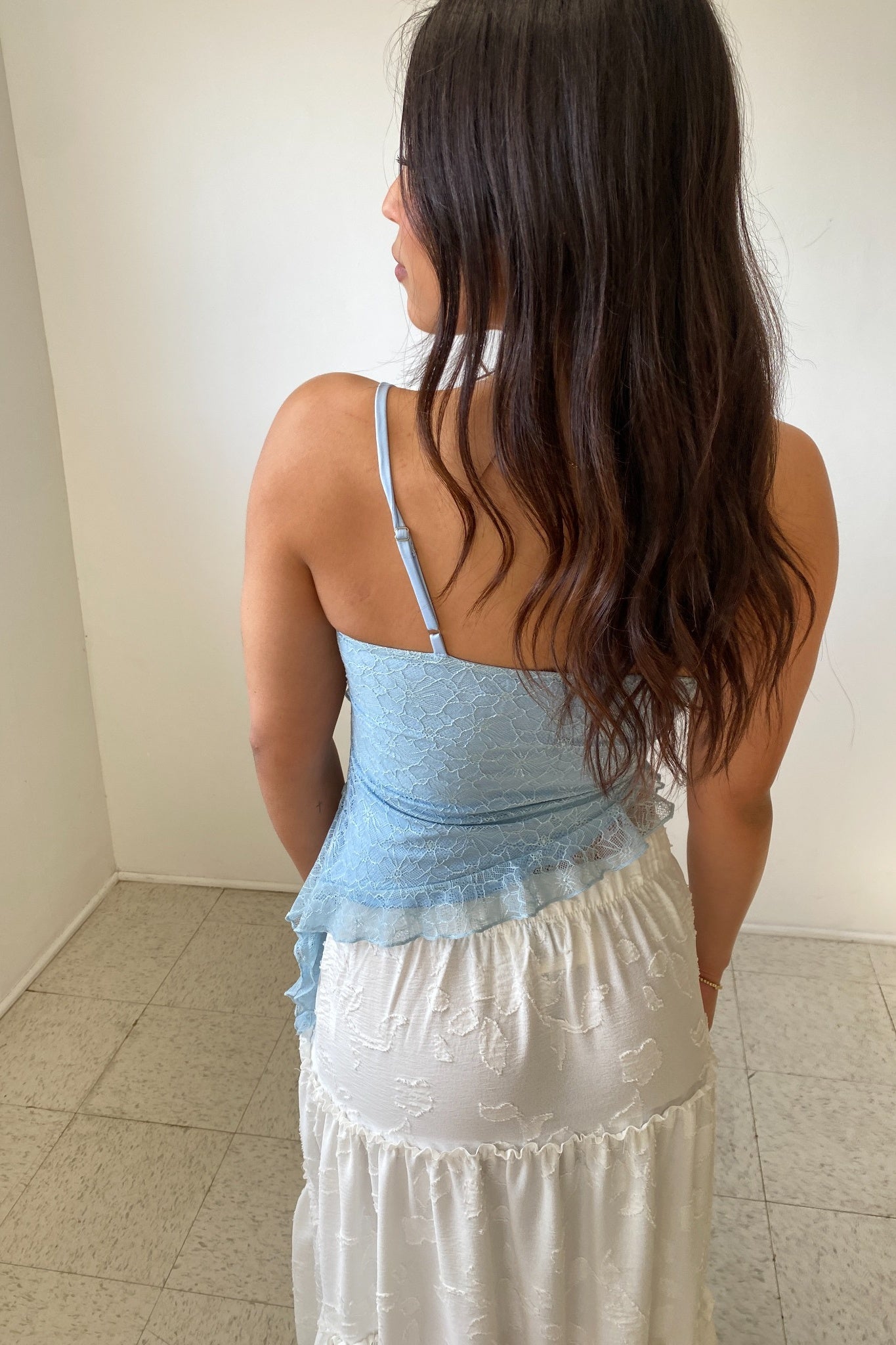 Woman wearing a light blue top and white skirt standing in a room with tiled floor.