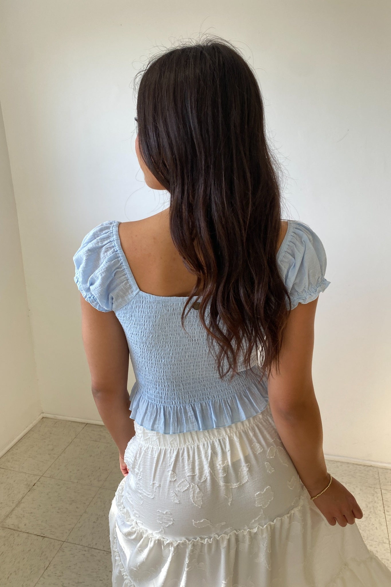 Woman wearing a light blue top and white skirt against a plain background