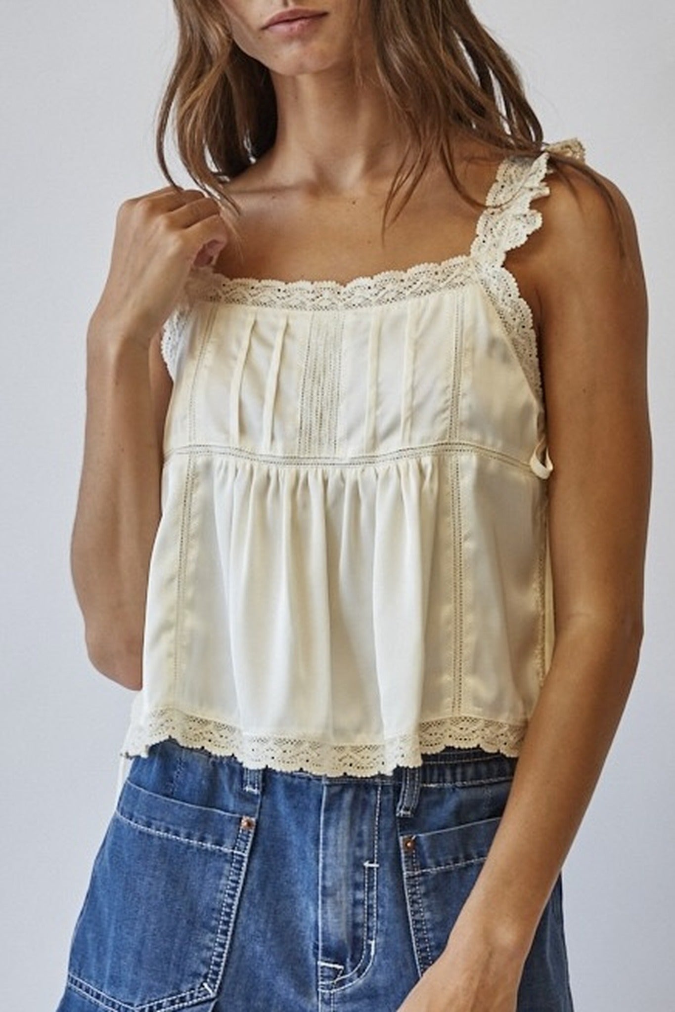 Woman wearing a cream lace-trimmed top and blue denim skirt against a plain background