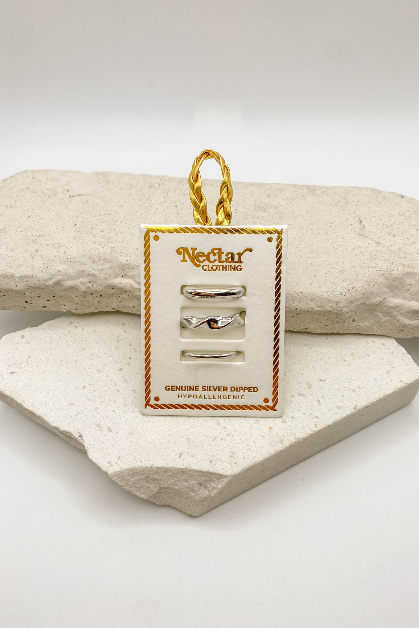 Gold jewelry set on a branded card with 'Nectar Clothing' logo, displayed on a textured surface.
