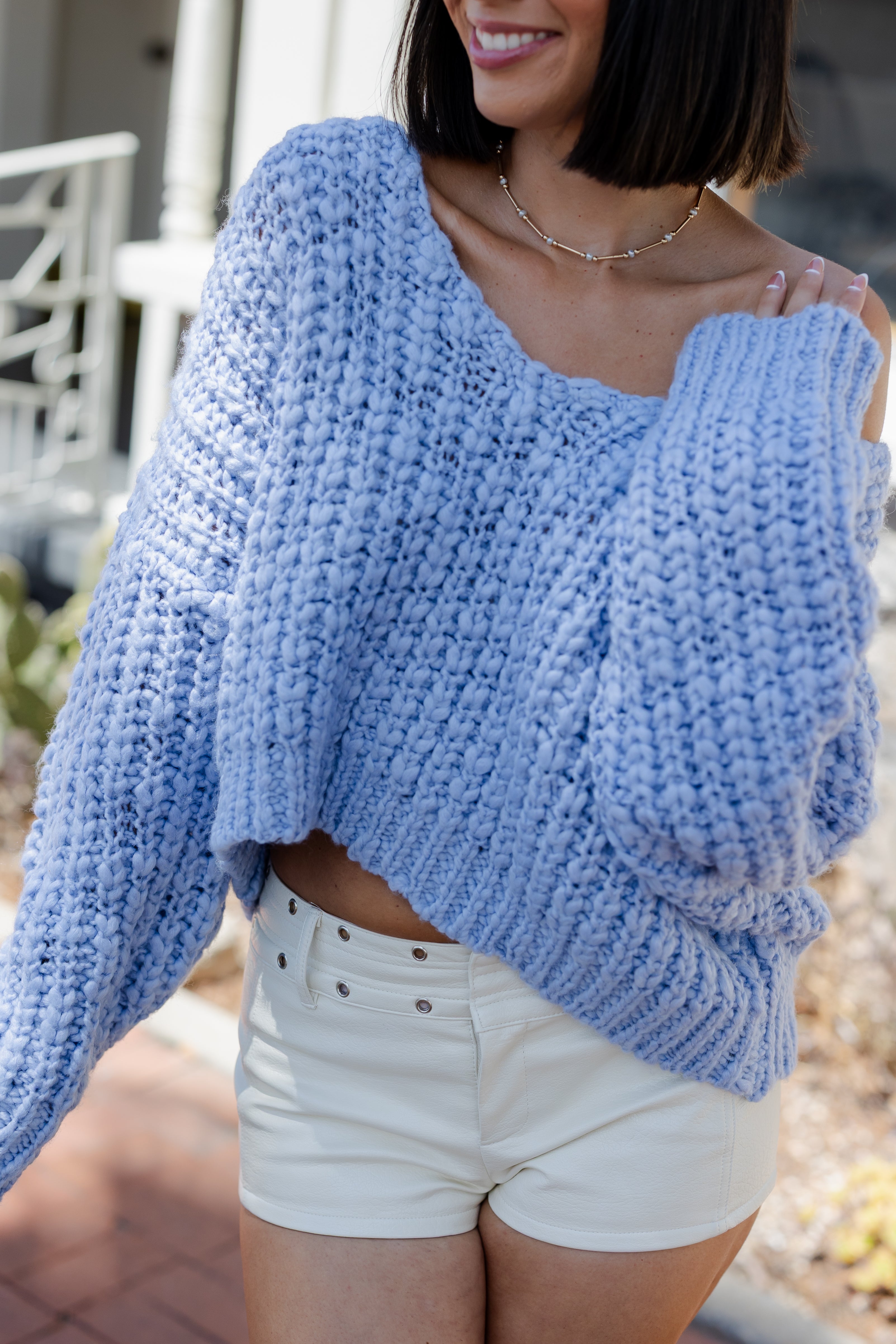 Woman wearing a blue knitted sweater and white shorts outdoors.