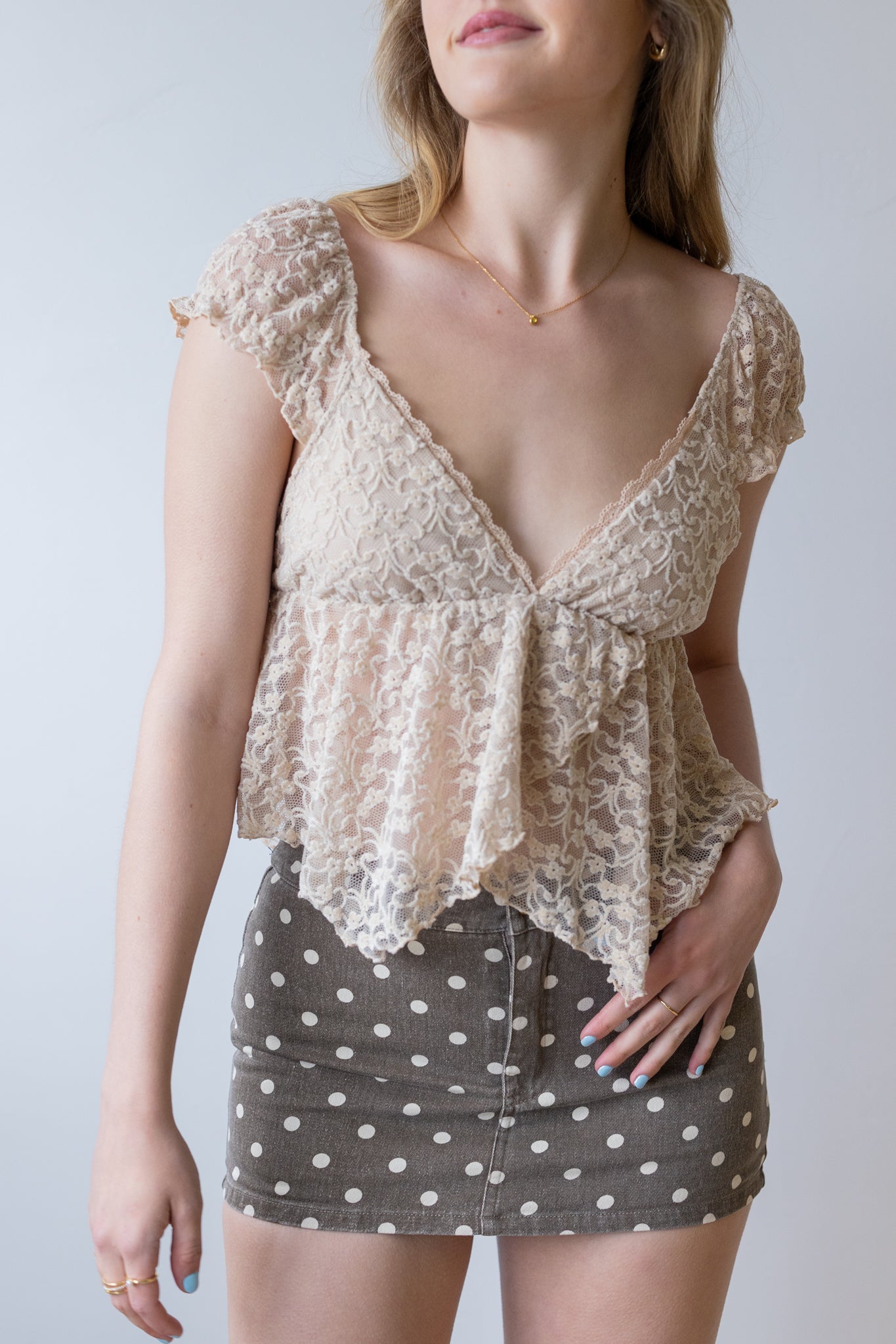 Woman wearing a beige lace top and polka dot skirt against a plain background