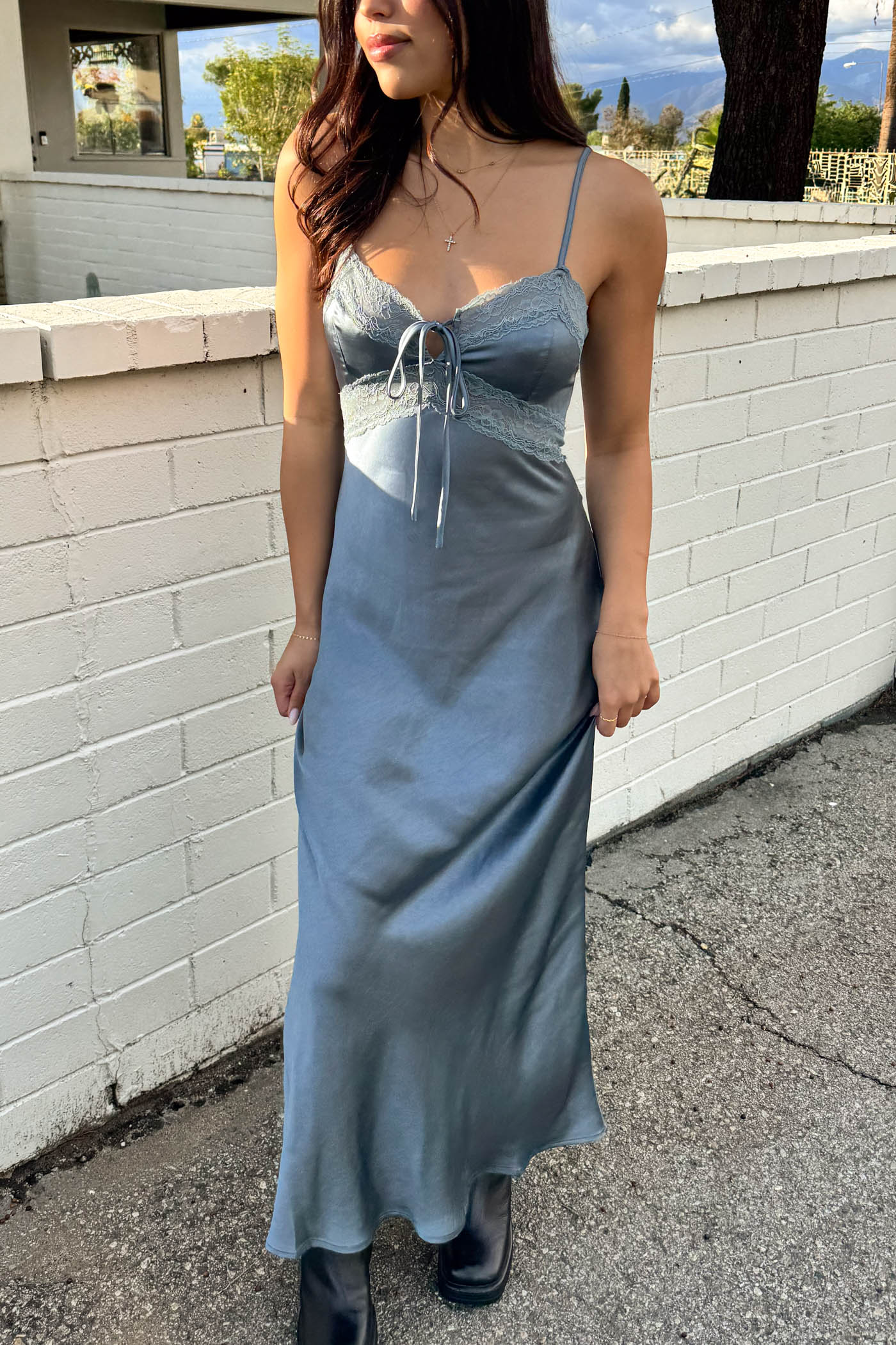 Woman wearing a light blue satin dress standing against a white brick wall.
