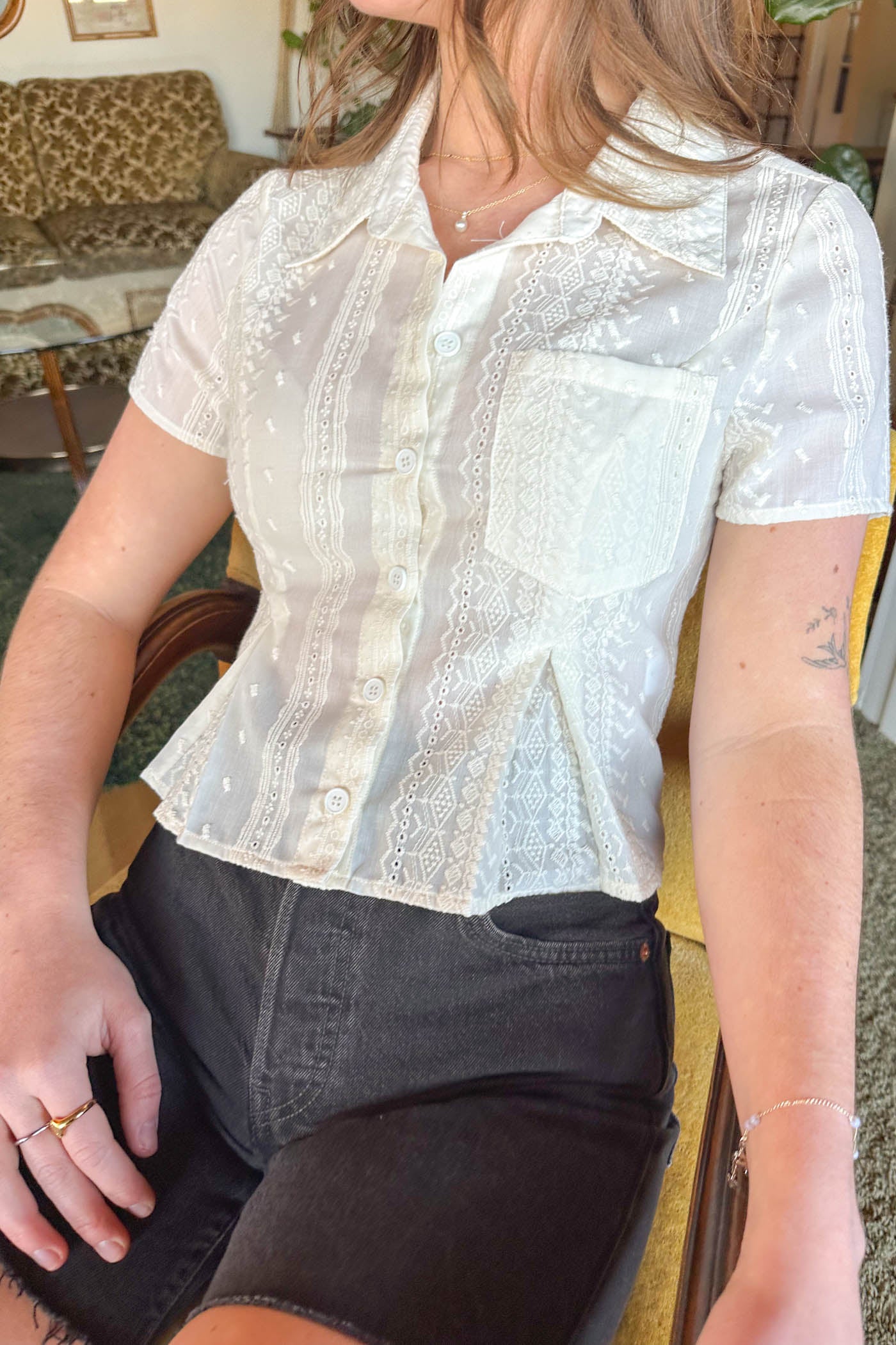 Person wearing a white lace blouse sitting on a couch.