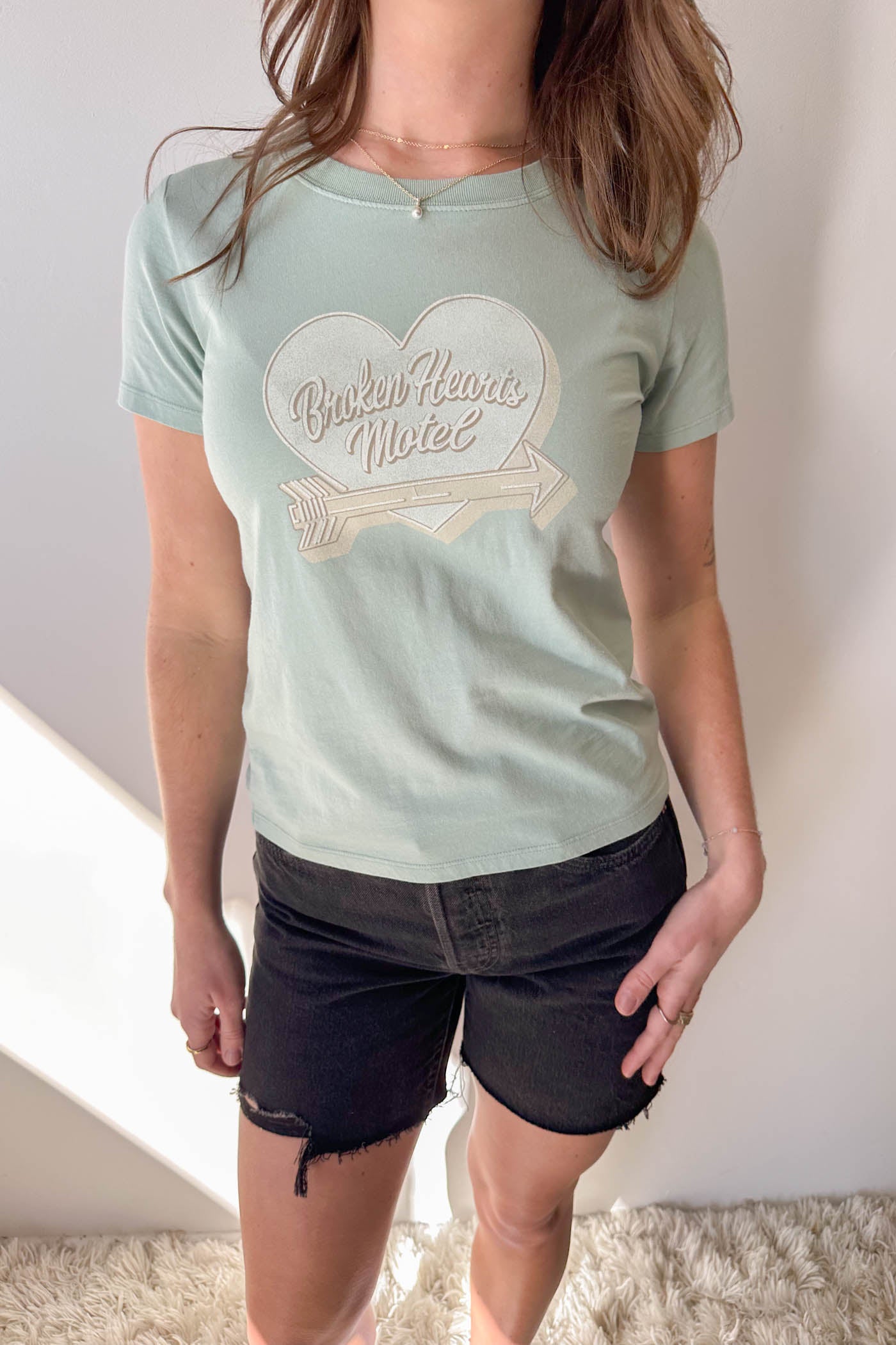 Person wearing a light green t-shirt with a heart design and text.