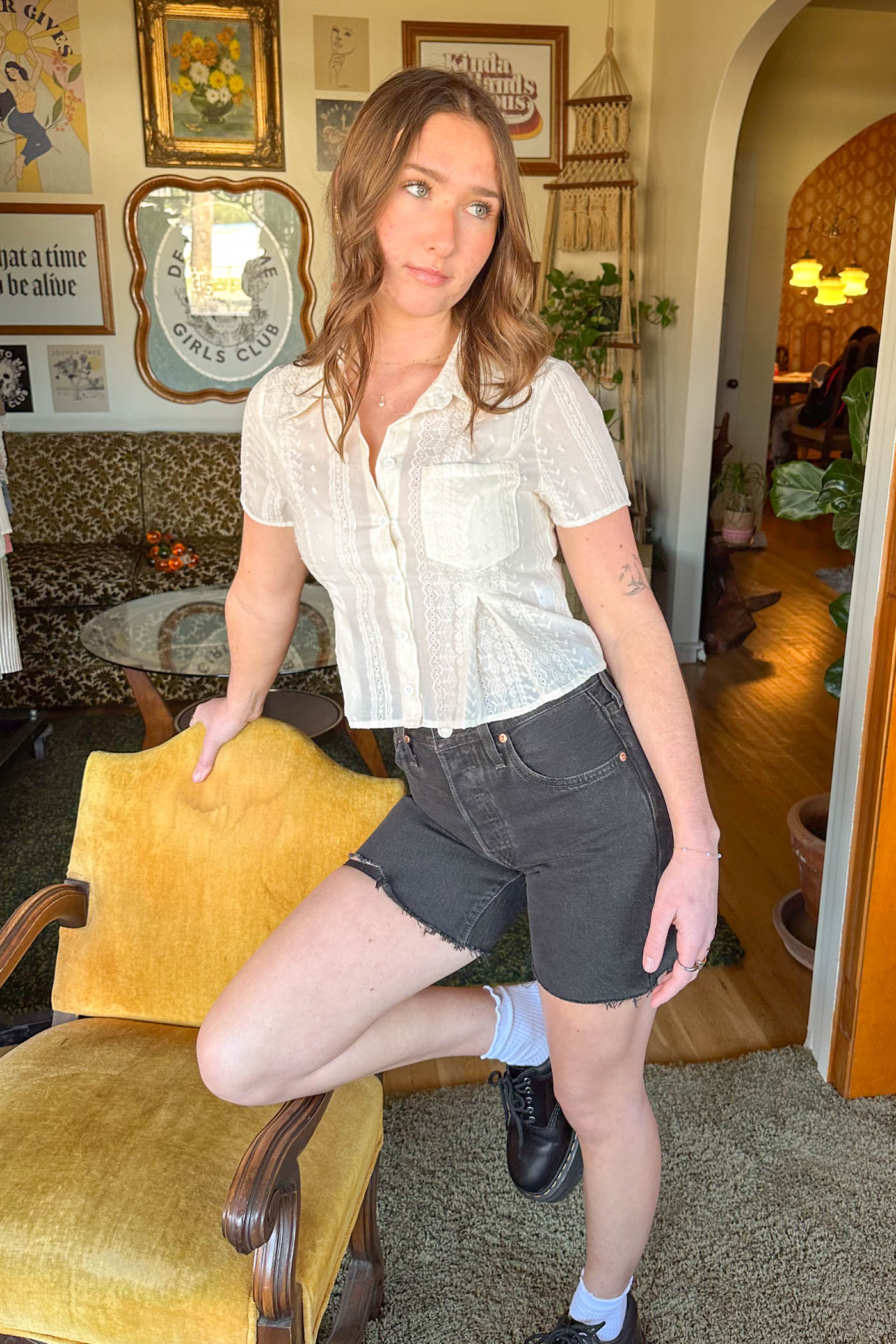 Woman in a white blouse and black shorts standing in a room with vintage decor.
