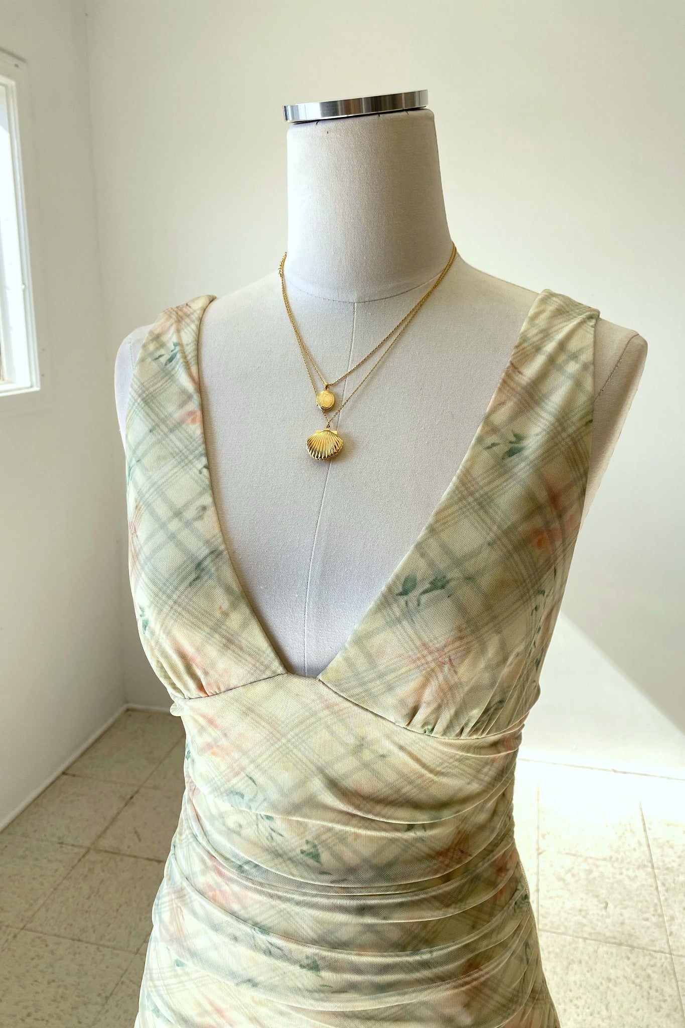 Mannequin wearing a patterned dress with a necklace on a plain background