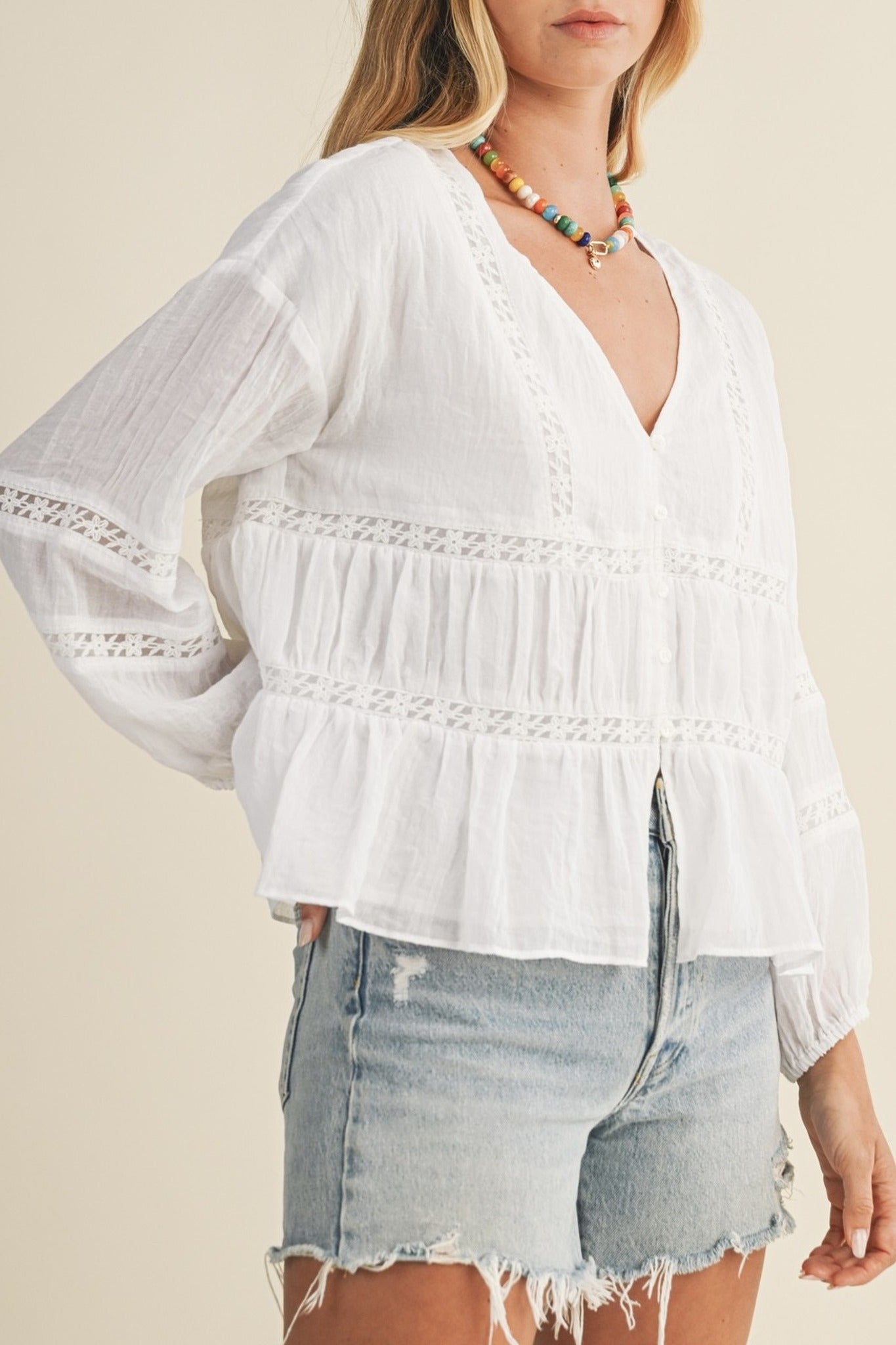 Woman wearing a white blouse with lace details and denim shorts on a beige background