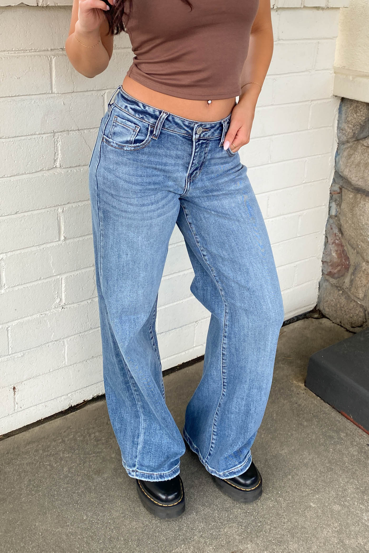 Person wearing blue jeans and a brown top against a white brick wall.