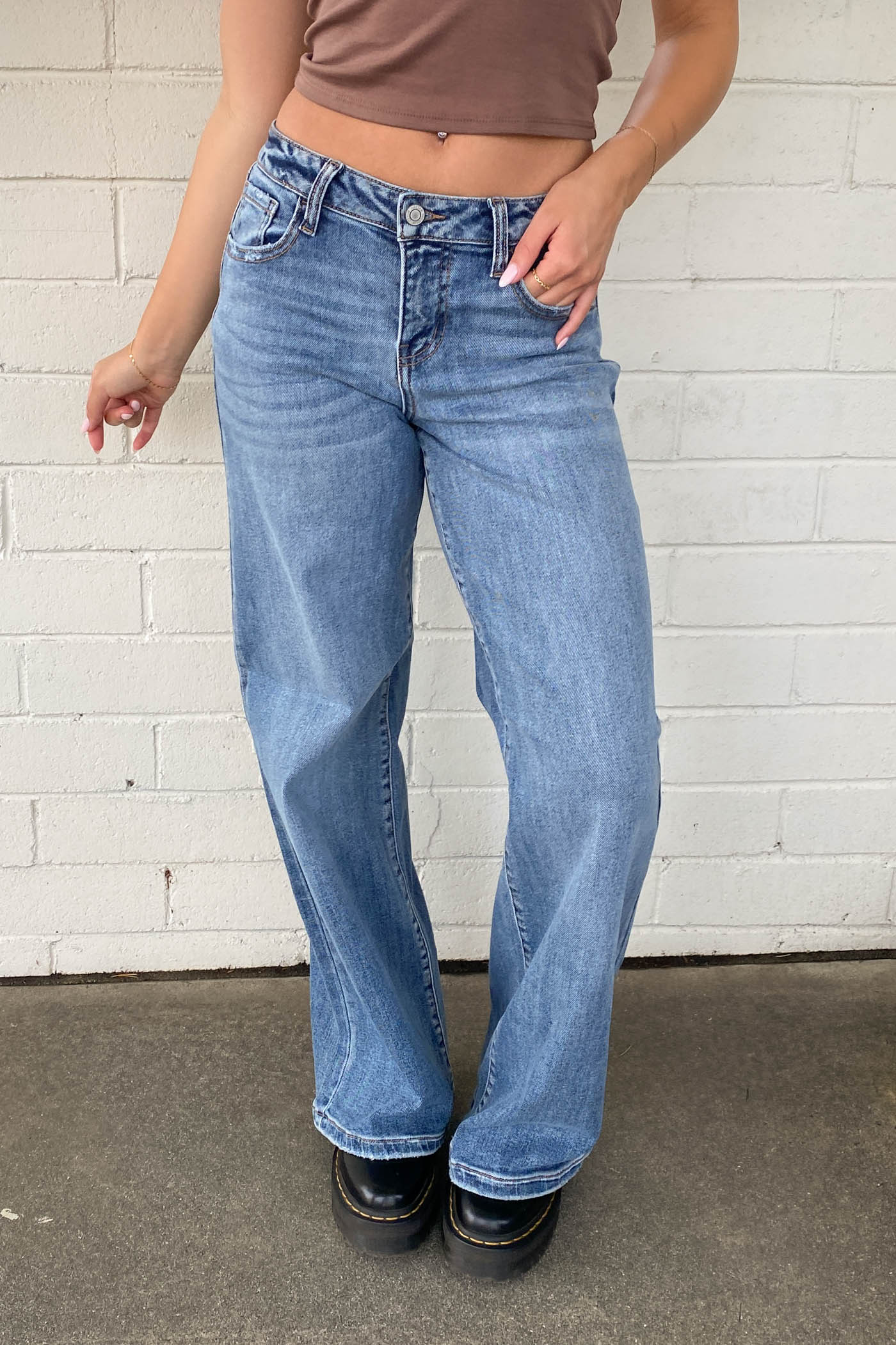 Person wearing blue jeans standing against a white brick wall.
