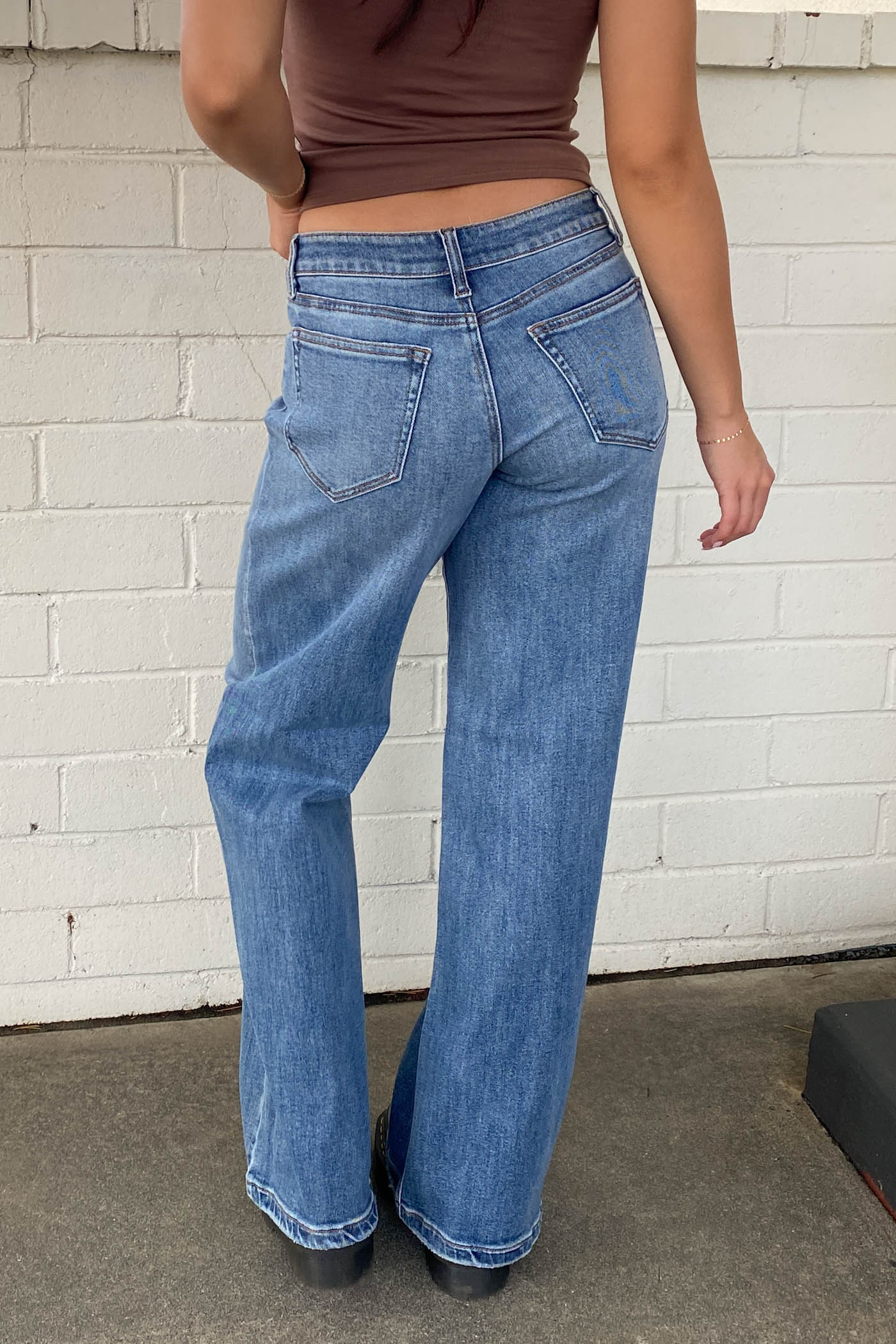 Person wearing blue jeans and a brown top against a white brick wall.