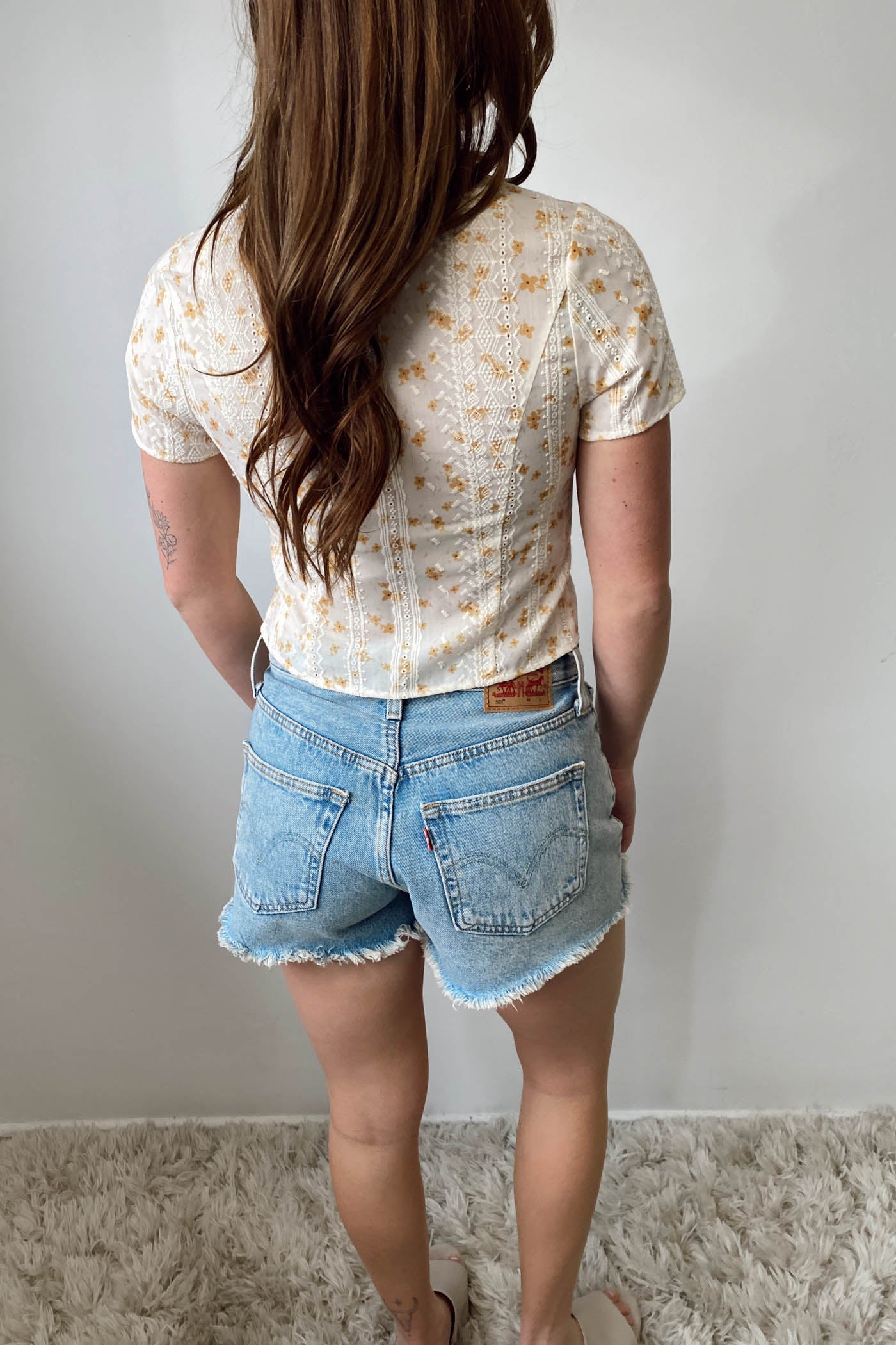 Person wearing a floral shirt and denim shorts against a plain background
