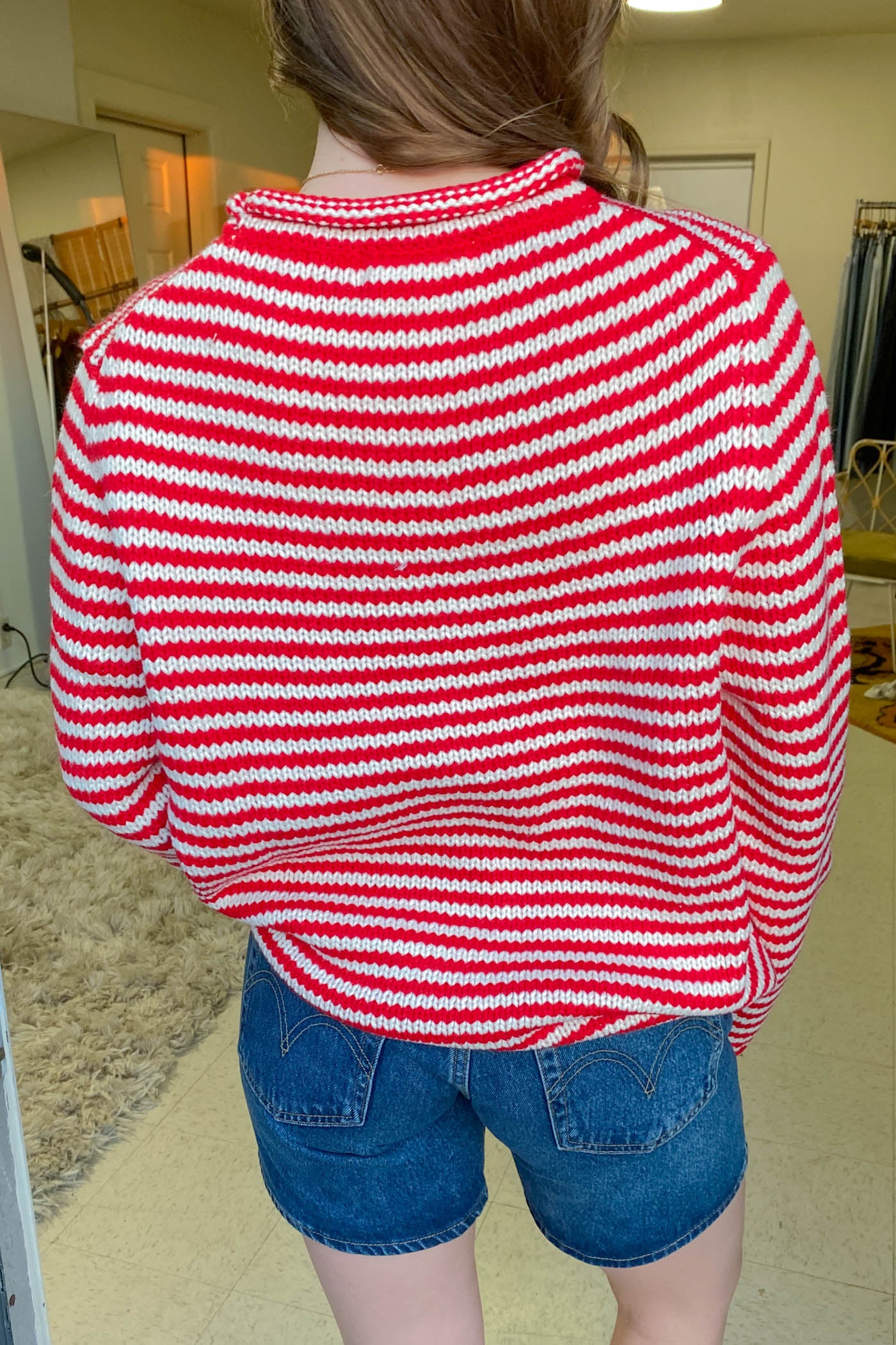 Person wearing a red and white striped sweater and blue shorts indoors.