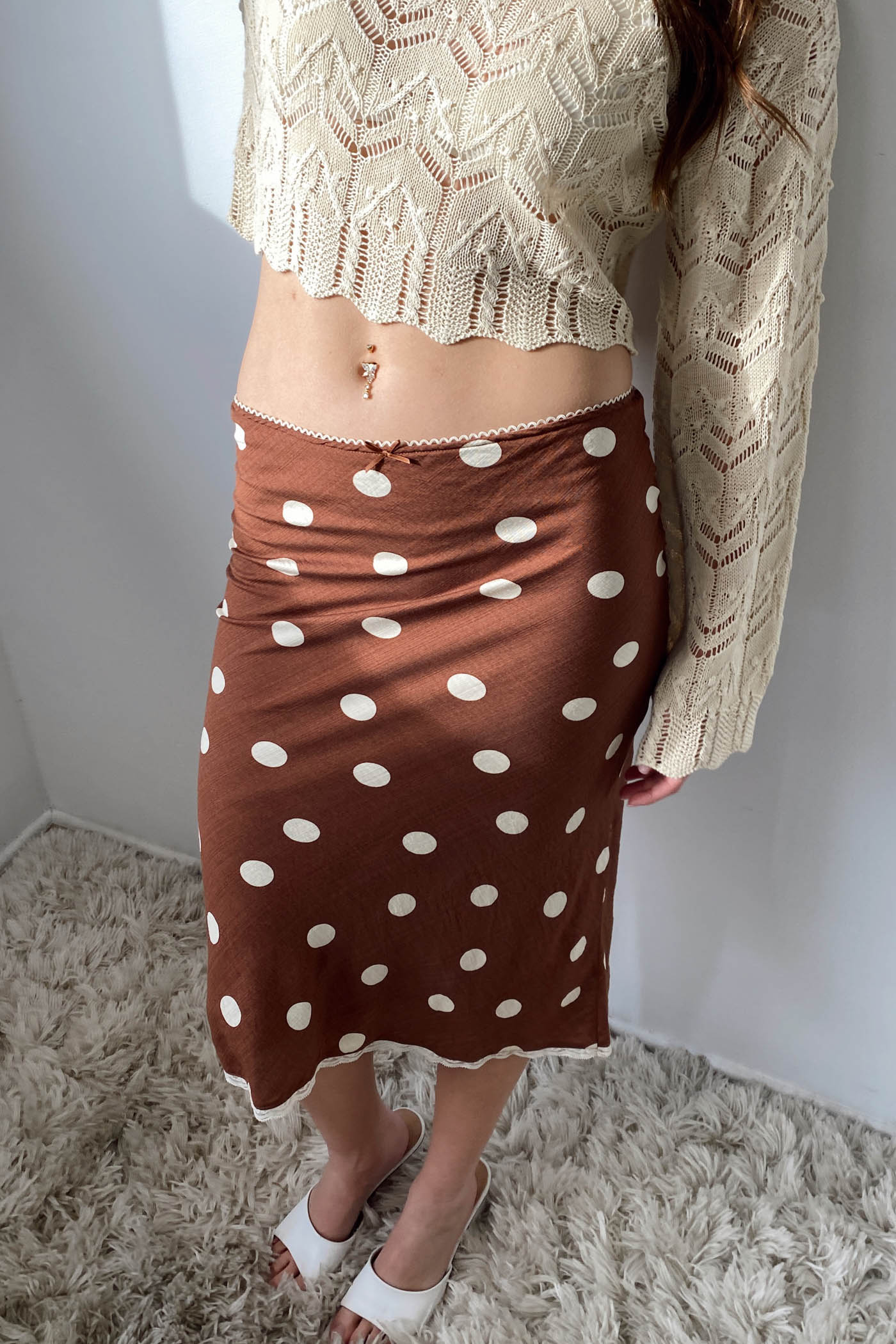 Person wearing a brown polka dot skirt and beige top against a plain background