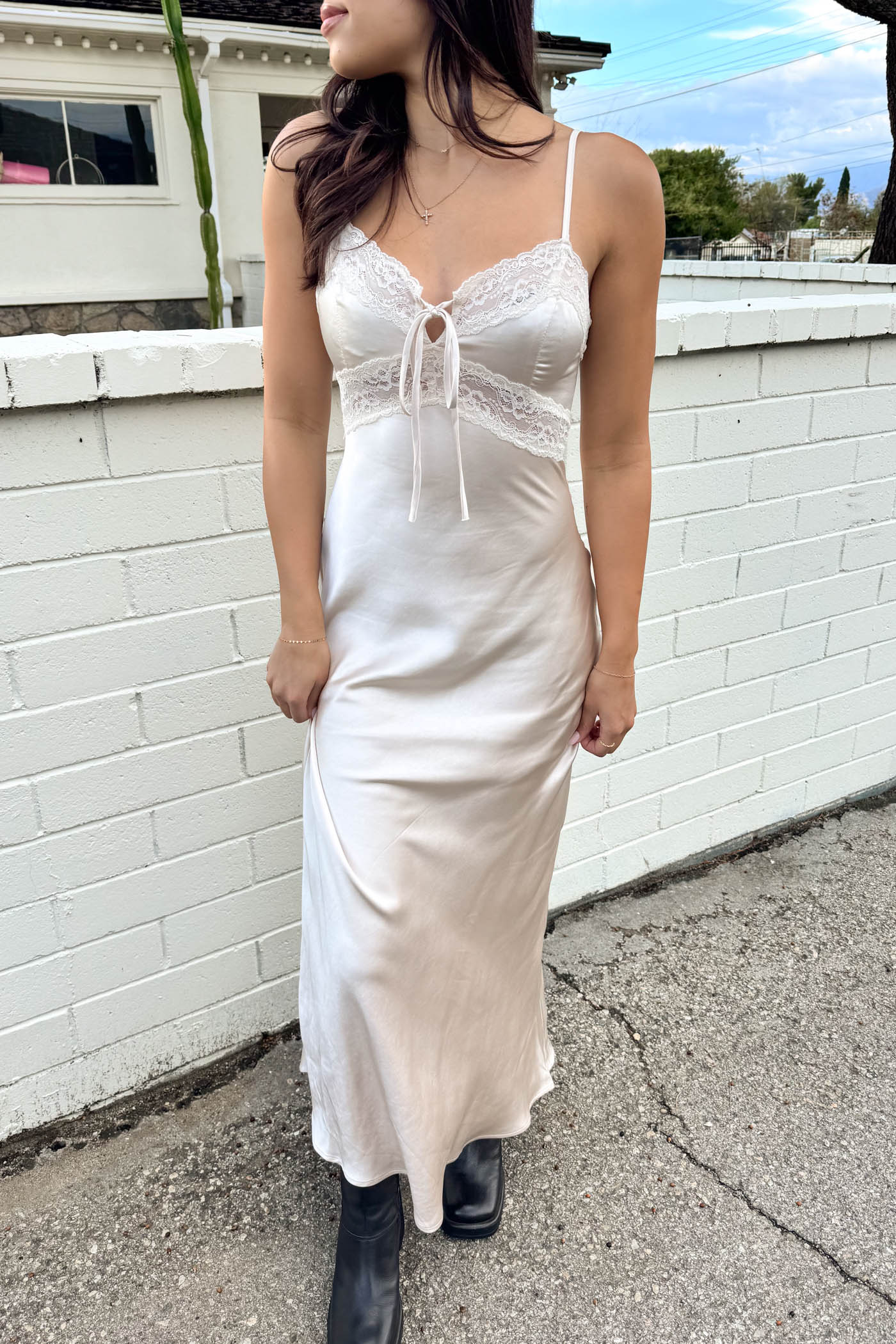 Woman wearing a white slip dress standing against a white brick wall.