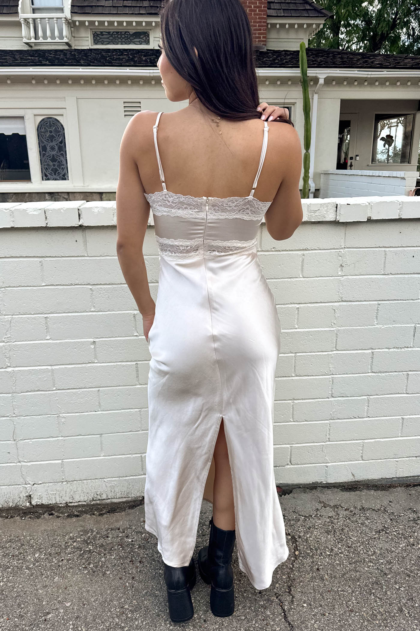 Woman wearing a white dress with a lace top and satin skirt, standing in front of a white brick wall.
