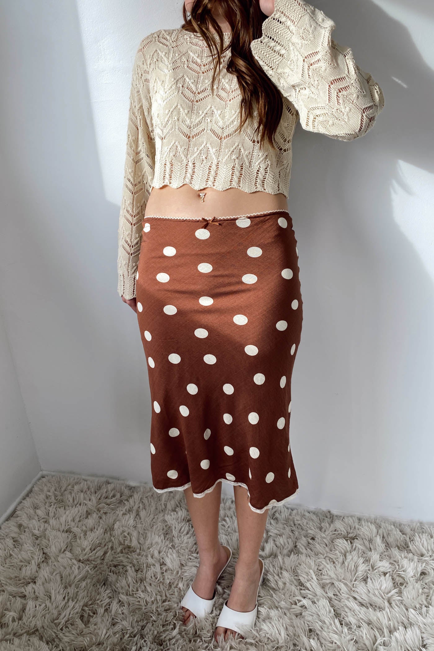 Person wearing a beige cable knit sweater and brown polka dot skirt on a white background