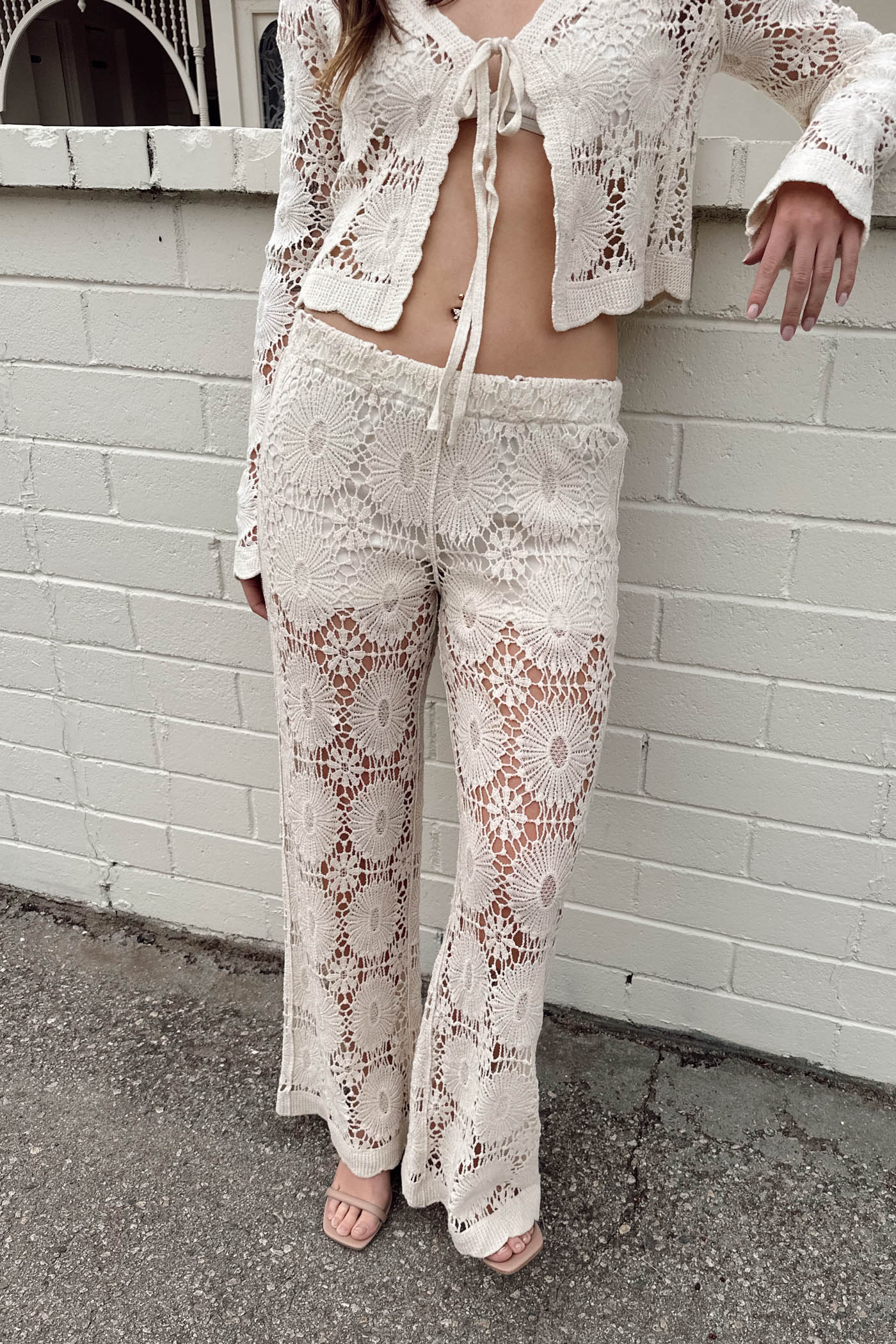 Person wearing a white lace outfit standing against a white brick wall.