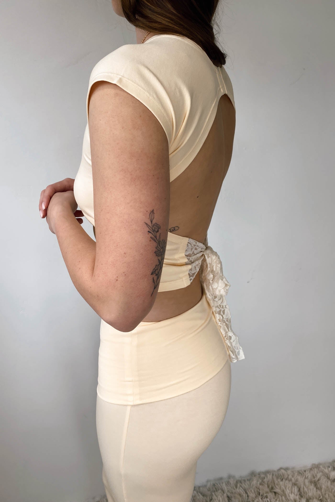 Person wearing a beige backless dress with lace details against a plain background