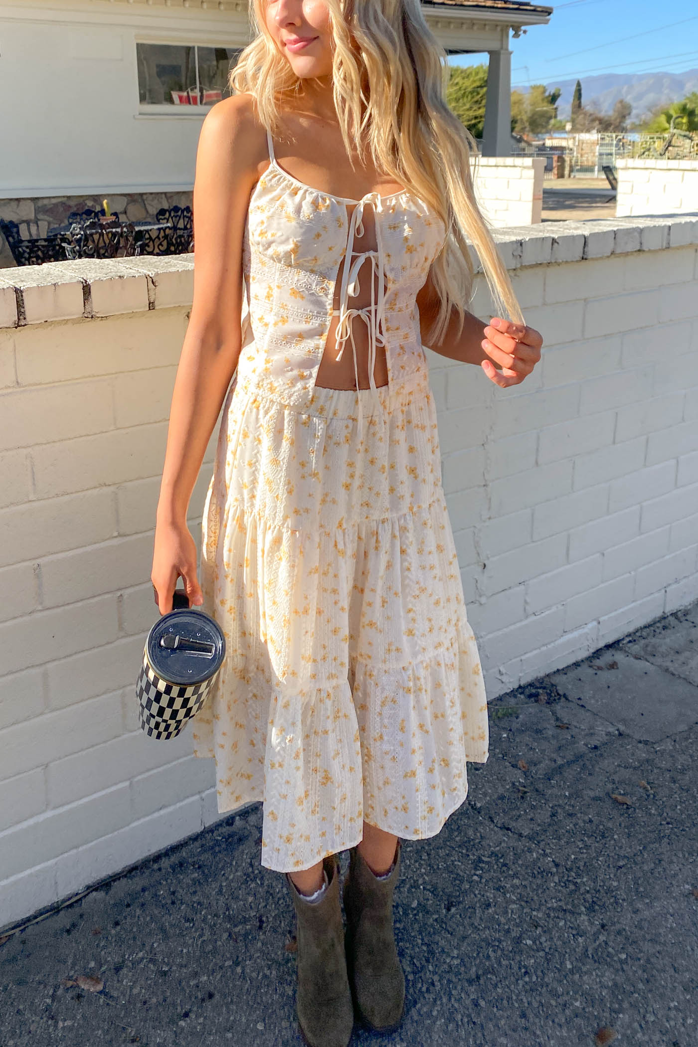 Woman in a white floral dress holding a black handbag against a white wall.